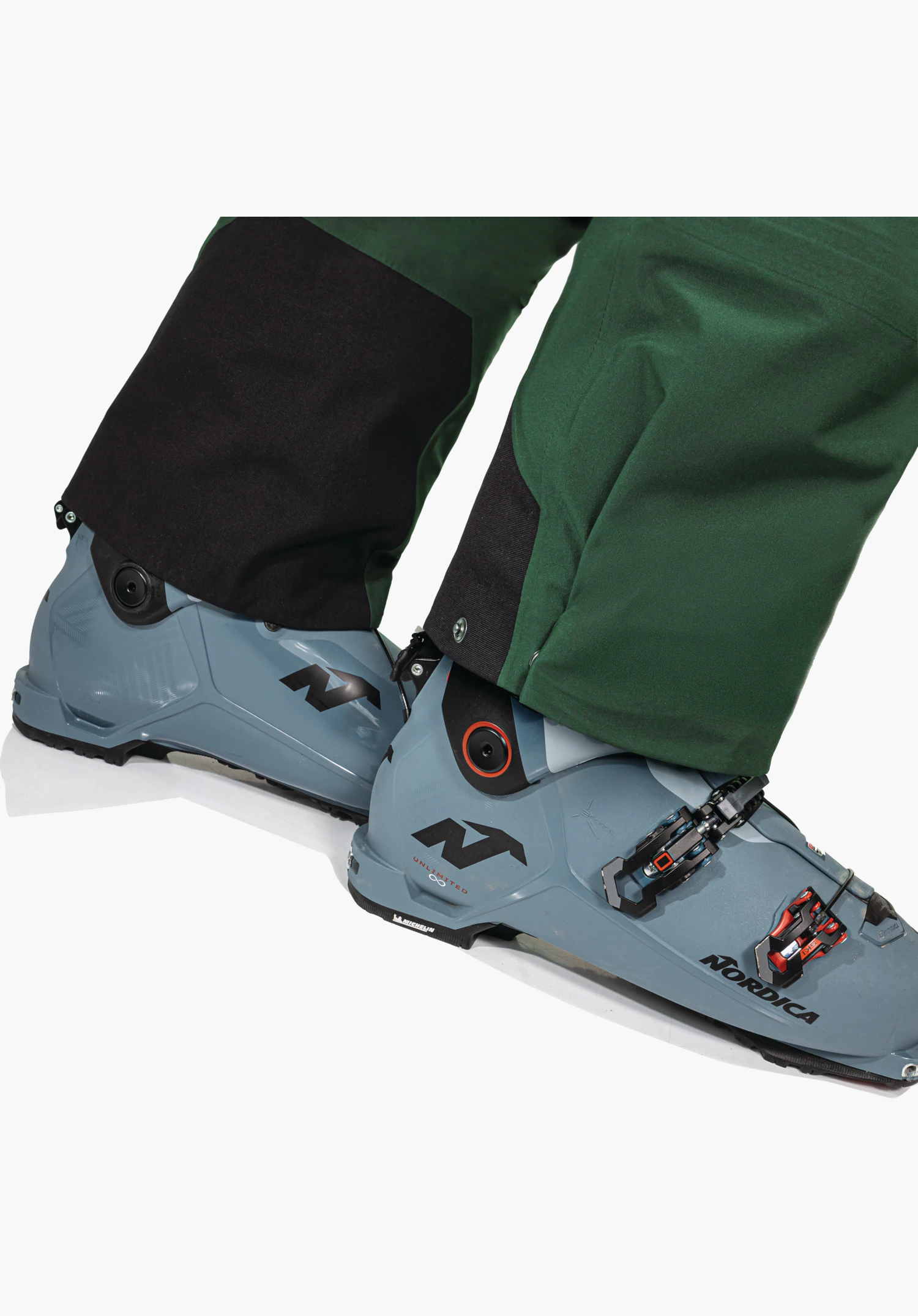 Pants Style Milagle MNS features the durable black edge protection at the bottom hem of the green leg, worn over ski boots. Close-up against a white background.
