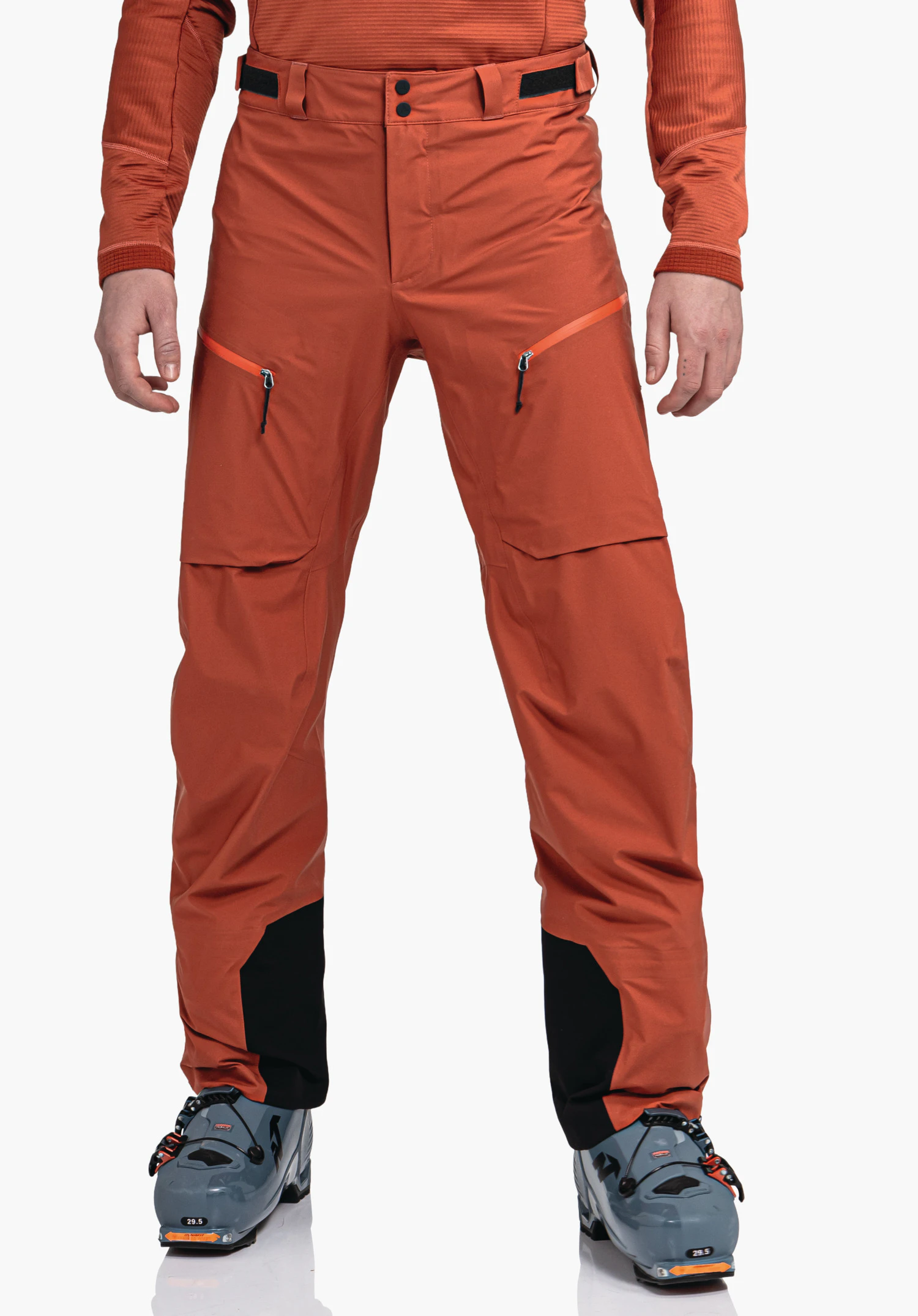 Pants Style Milagle MNS donkeroranje skibroek, gedragen, met diagonale ritszakken en zwarte enkelverstevigingen; handen zichtbaar, persoon staat voor een neutrale achtergrond.
