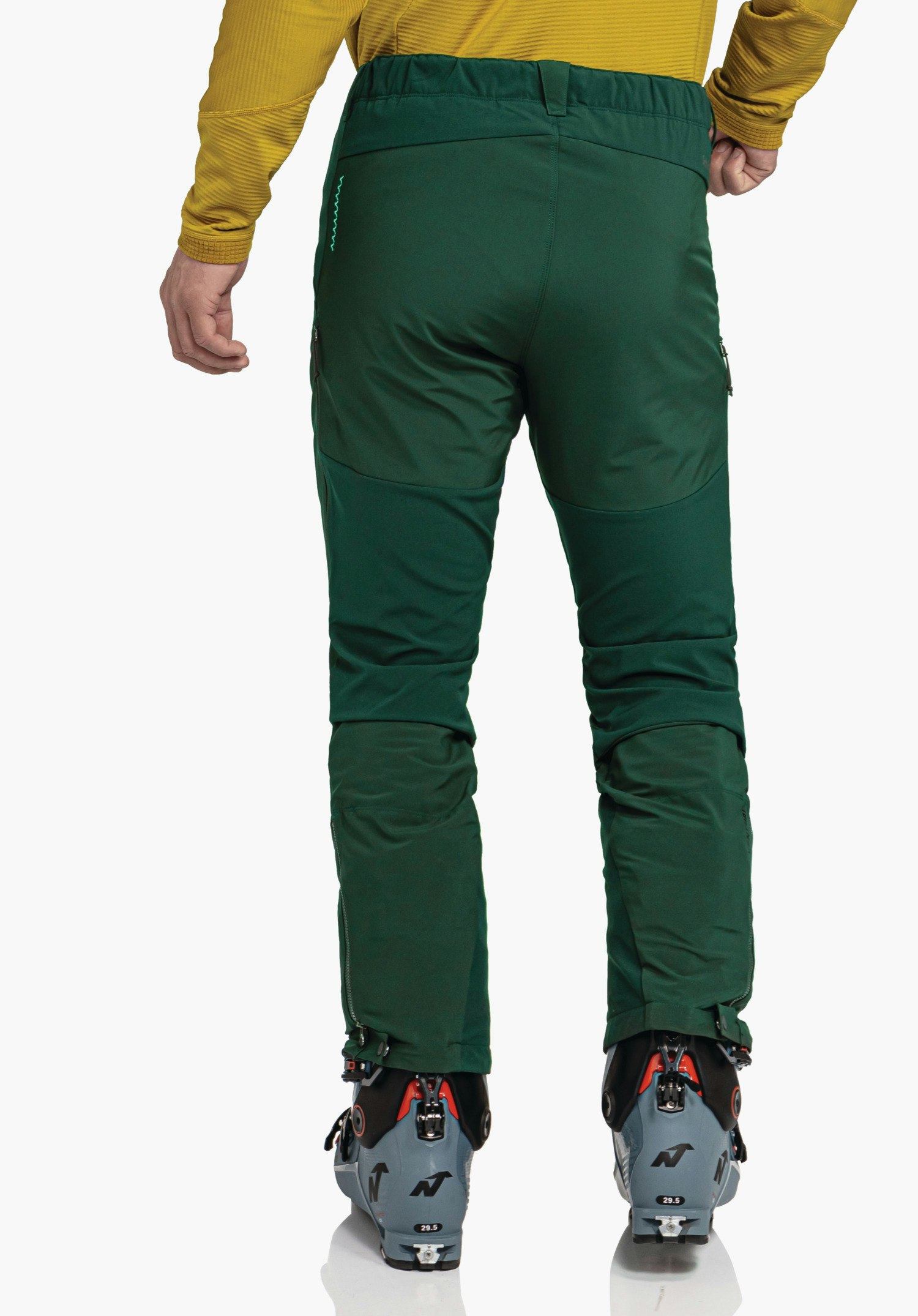 Softshell Pt Style Milagle MNS pantalon de ski vert foncé, porté de dos par une personne; posture debout sur fond blanc avec chaussures de ski, haut jaune clair visible. Texte: 29.5
