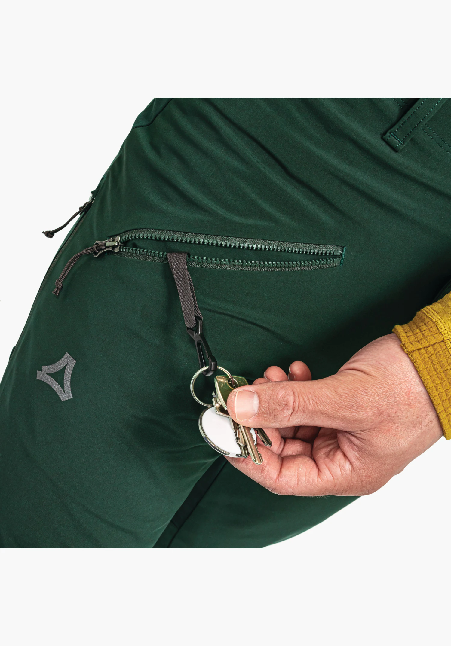 Softshell Pt Style Milagle MNS shows the open zip pocket on the green softshell fabric with an integrated key clip holding keys, as well as the Schöffel logo as a close-up against a white background.