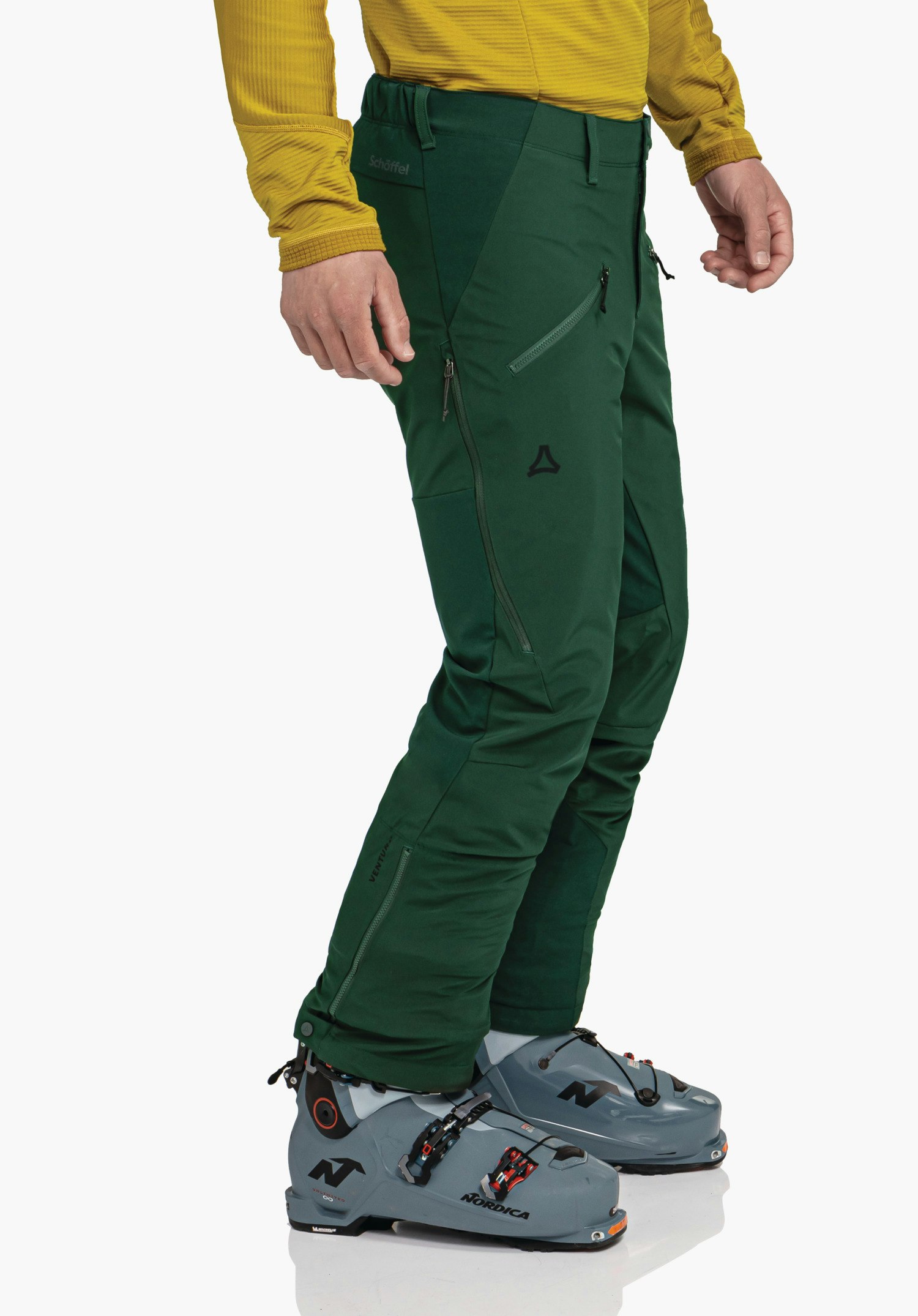 Softshell Pt Style Milagle MNS pantalon de ski vert foncé porté par une personne debout; haut jaune clair et chaussures de ski grises devant fond studio blanc. Texte: "Schöffel", "VENTURI", "NORDICA". Logo Schöffel visible.