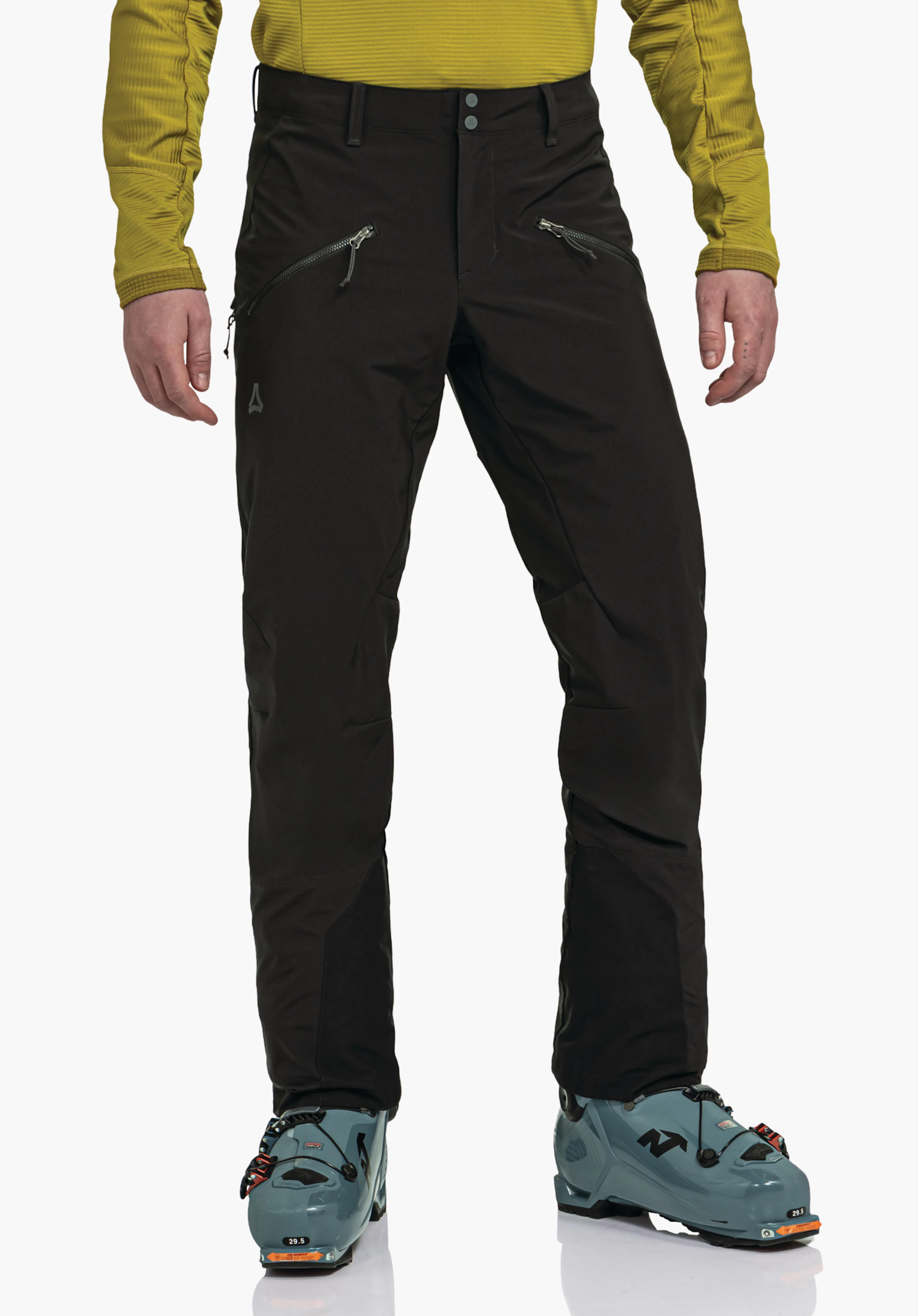 Softshell Pt Style Milagle MNS pantalon noir, porté par une personne debout devant un fond blanc; poches zippées frontales, logo Schöffel sur la cuisse gauche, haut jaune clair, chaussures de ski bleues; texte: «29.5».