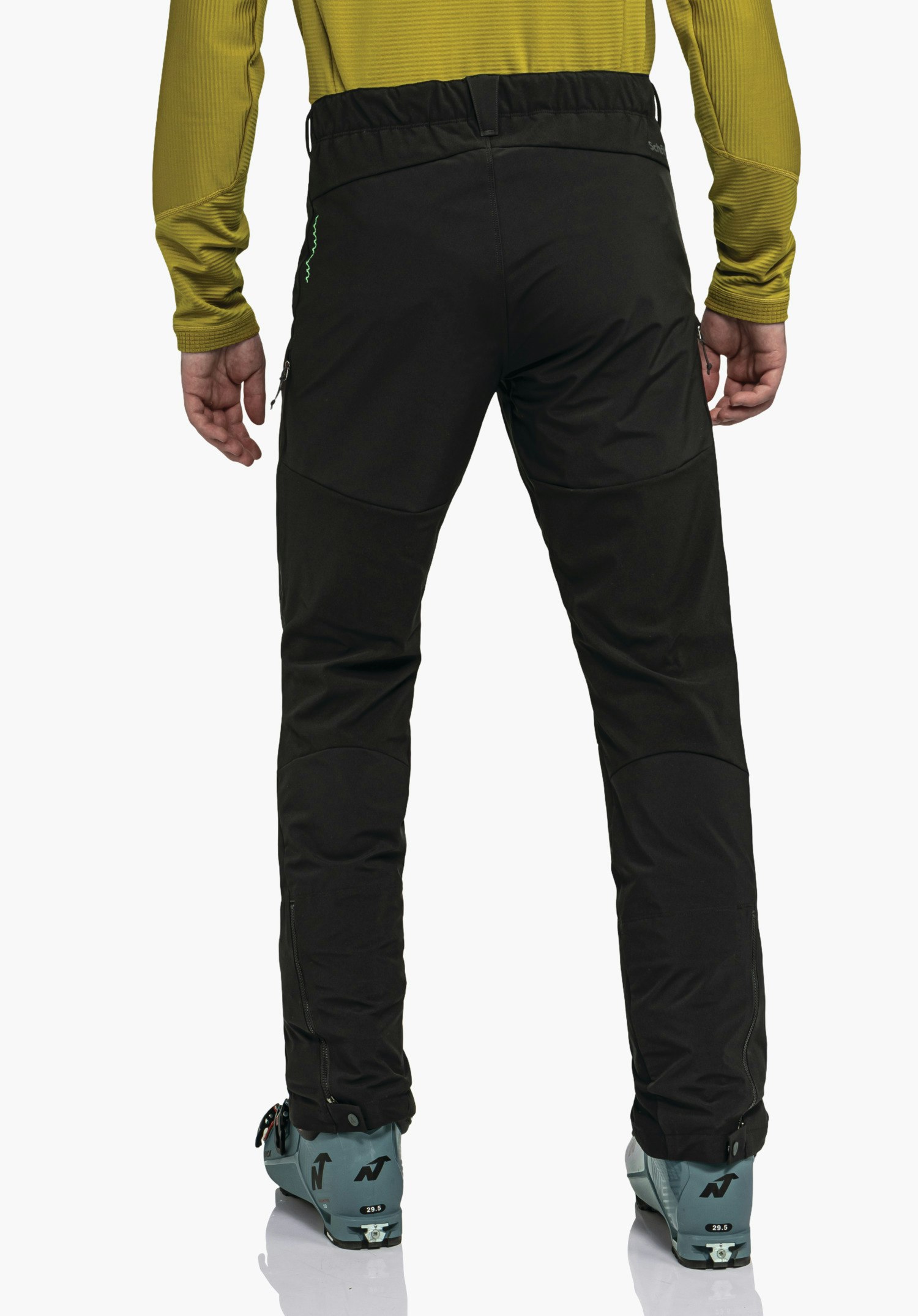 Softshell Pt Style Milagle MNS Schwarze Hose steht aufrecht, getragen von Person; dunkelgelbes Oberteil, hellblaue Skischuhe sichtbar; Studioaufnahme vor weißem Hintergrund.