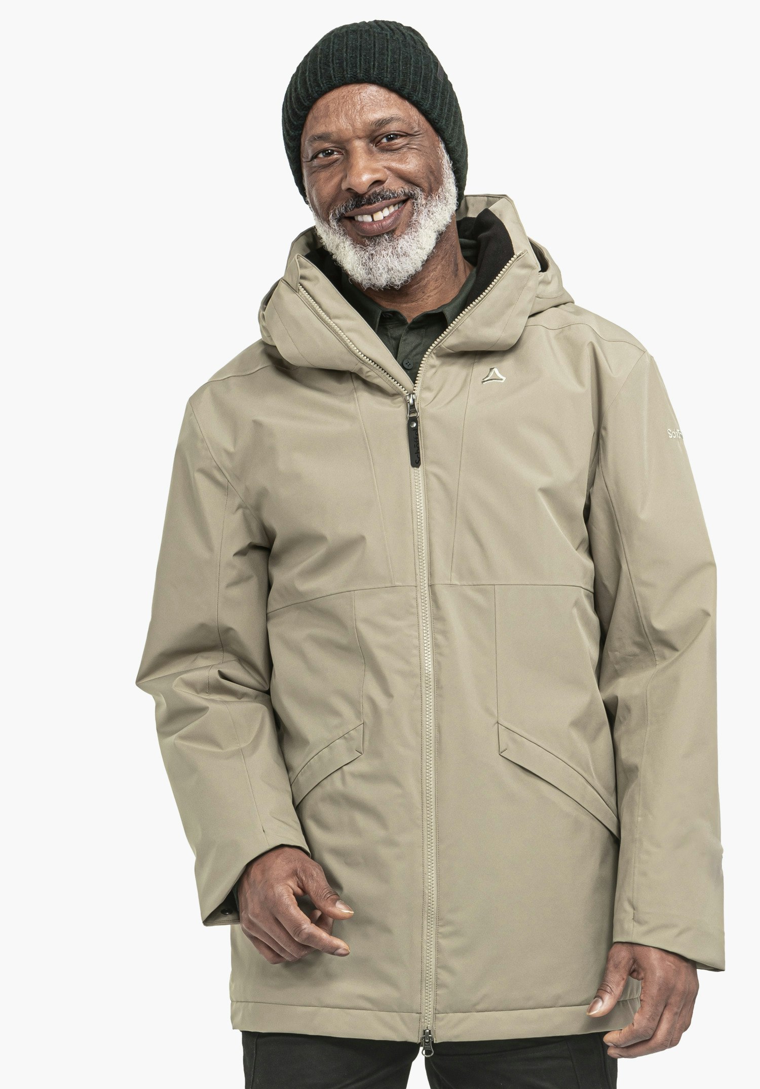Ins Parka Style Malkay MNS Mann im hellbraunen Parka mit Schöffel-Logo, lächelnd, steht vor neutralem hellem Hintergrund; trägt dunkelgrüne Mütze, weißem Bart und schwarze Hose.