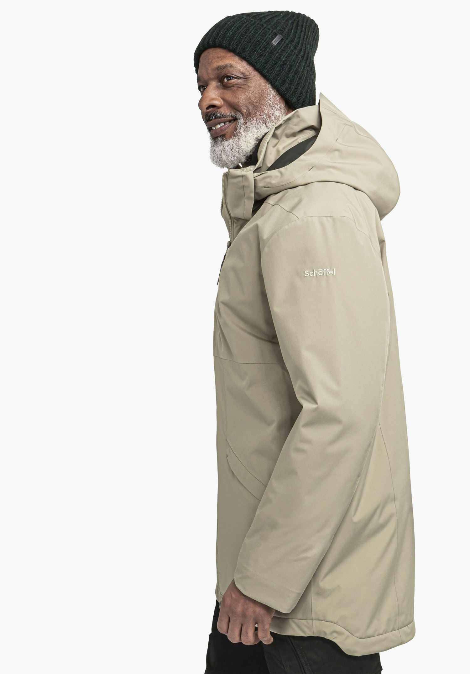 Ins Parka Style Malkay MNS Mann mit dunkelgrüner Mütze trägt Kapuzenjacke, steht im Profil und lächelt; neutraler weißer Hintergrund. Text auf Ärmel: "Schöffel".