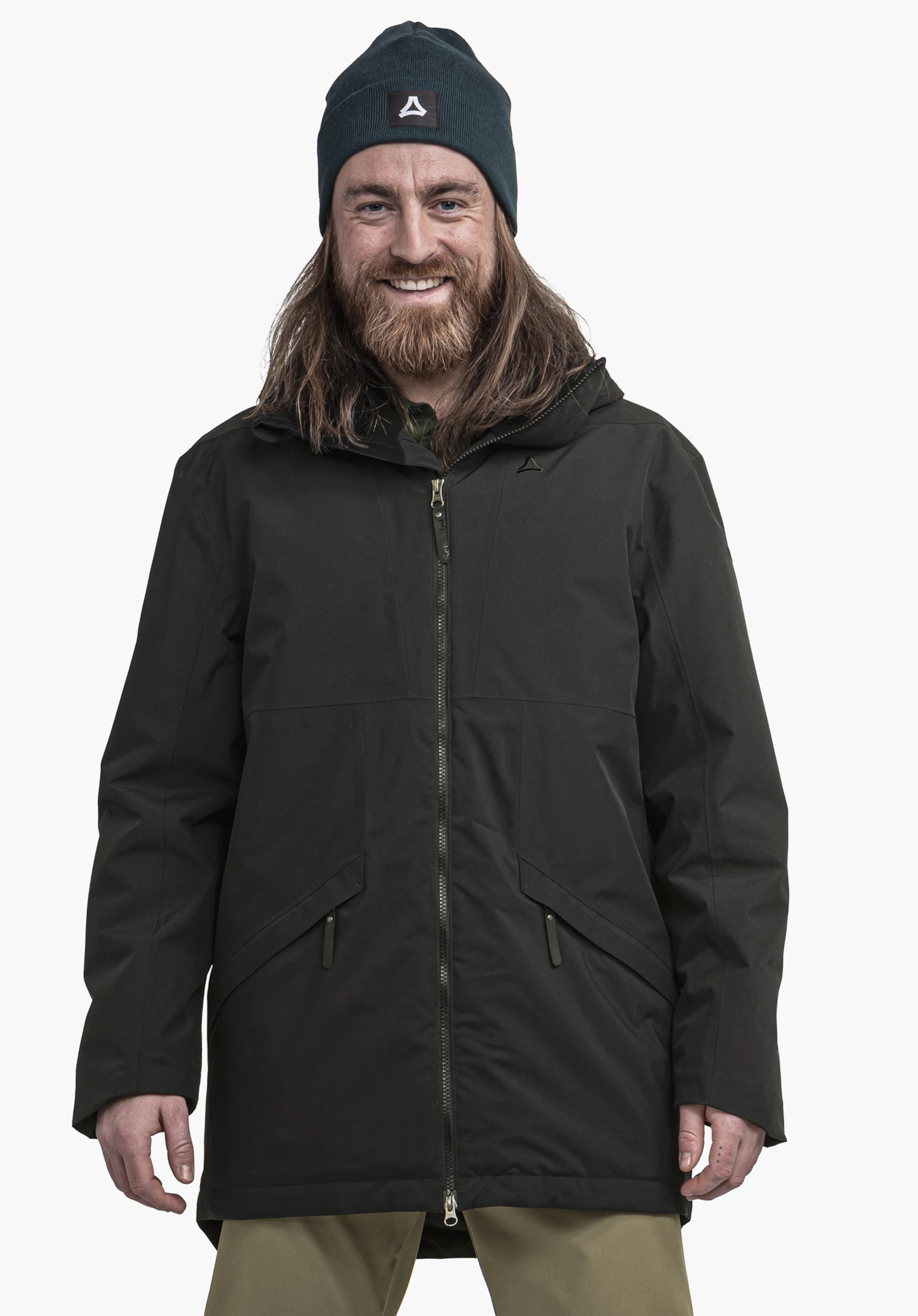 Ins Parka Style Malkay MNS Homme barbu portant une veste noire et un bonnet vert foncé avec logo Schöffel, souriant et debout de face devant un fond blanc.