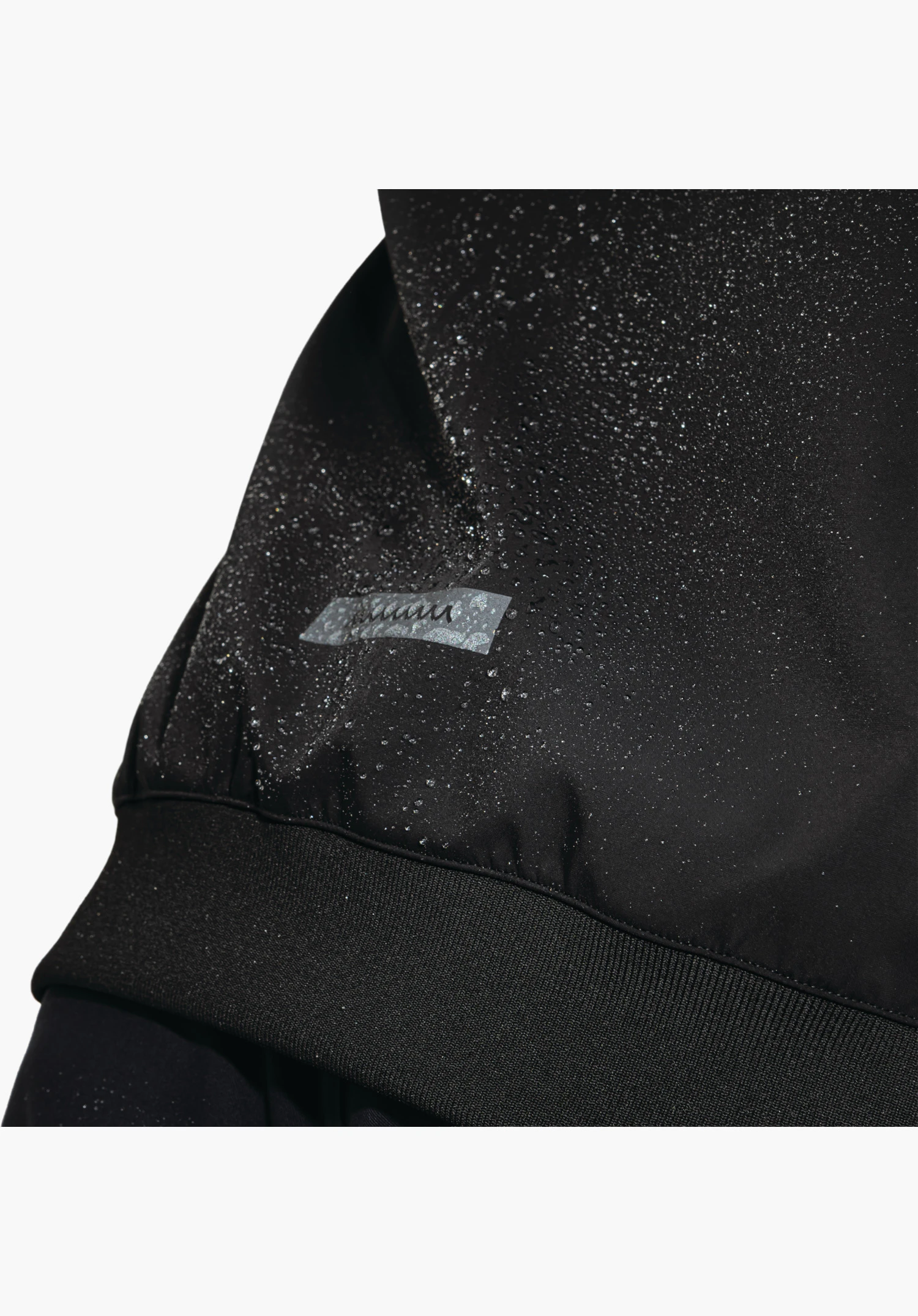 Softshell Jk Style Suavio MNS montre la surface déperlante en noir avec des gouttelettes d'eau perlantes et un bord-côte élastique, gros plan sur fond blanc.