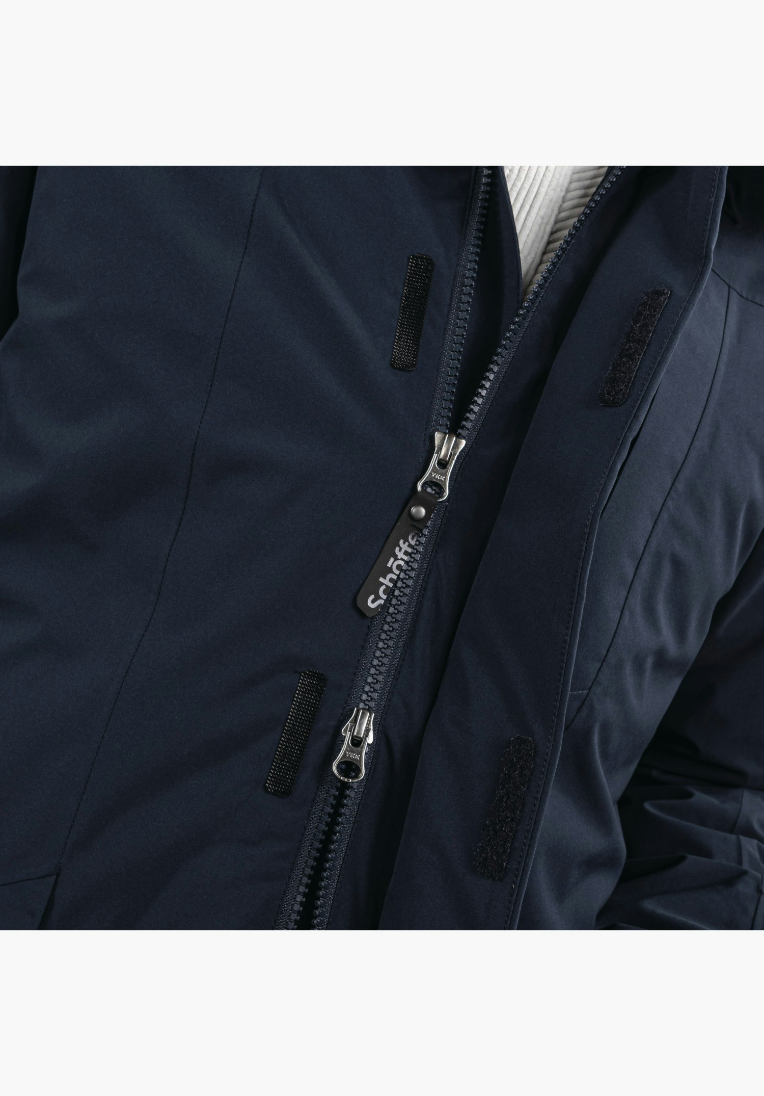 3in1 Parka Style Borkol MNS gedetailleerd aanzicht van de verborgen rits van de blauwe borstzak, waarbij een hand het functionele treklipje vasthoudt. Close-up tegen een witte achtergrond.