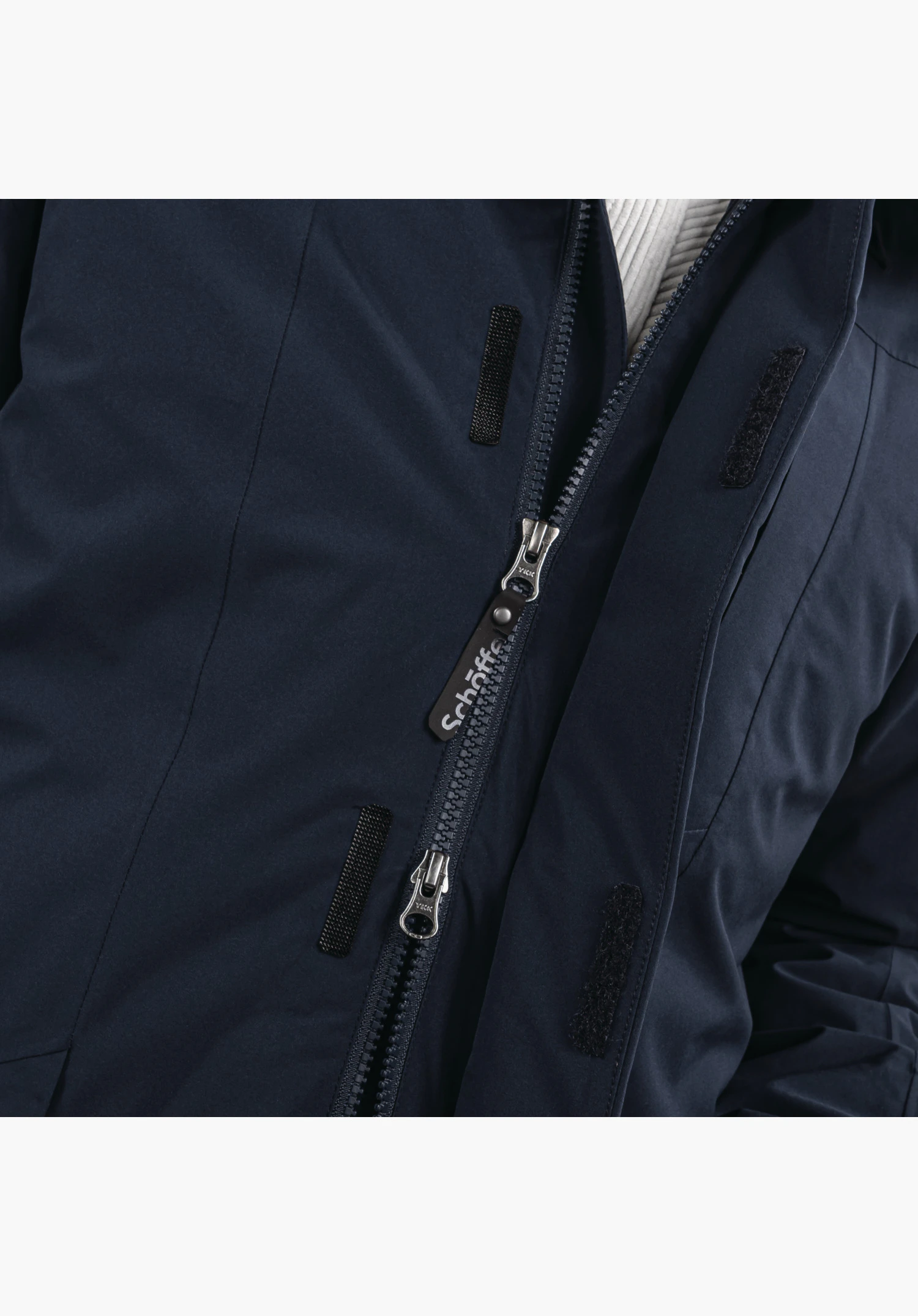 3in1 Parka Style Borkol MNS gedetailleerd aanzicht van de verborgen rits van de blauwe borstzak, waarbij een hand het functionele treklipje vasthoudt. Close-up tegen een witte achtergrond.