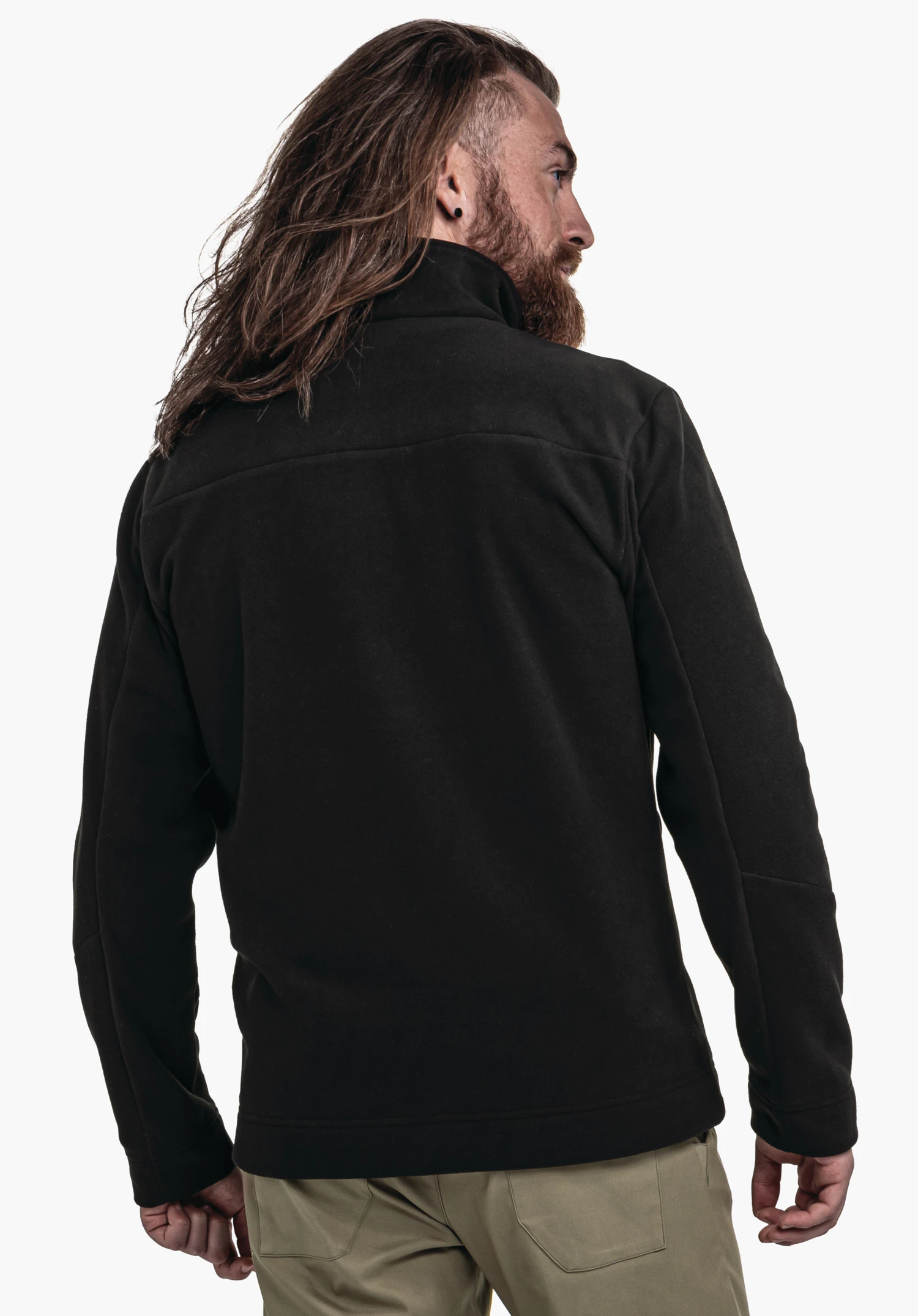 Fleece Jk Style Karif MNS Dunkel schwarze Jacke, Mann trägt sie, steht mit dem Rücken zum Betrachter vor hellem Studiohintergrund. Langes braunes Haar, Bart, hellgrüne Hose.