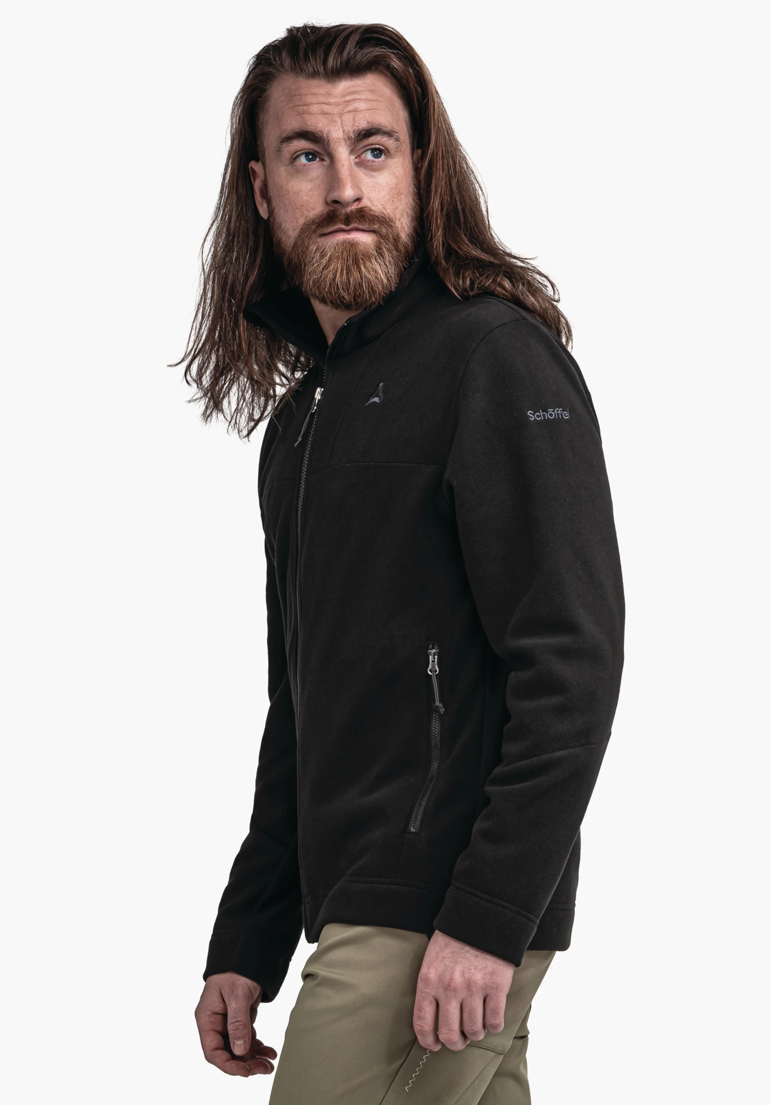 Fleece Jk Style Karif MNS Schwarze Fleecejacke mit Schöffel-Logo und Schriftzug "Schöffel", getragen von Mann mit langem braunem Haar und braunem Bart, Blick nach oben links, vor weißem Hintergrund.