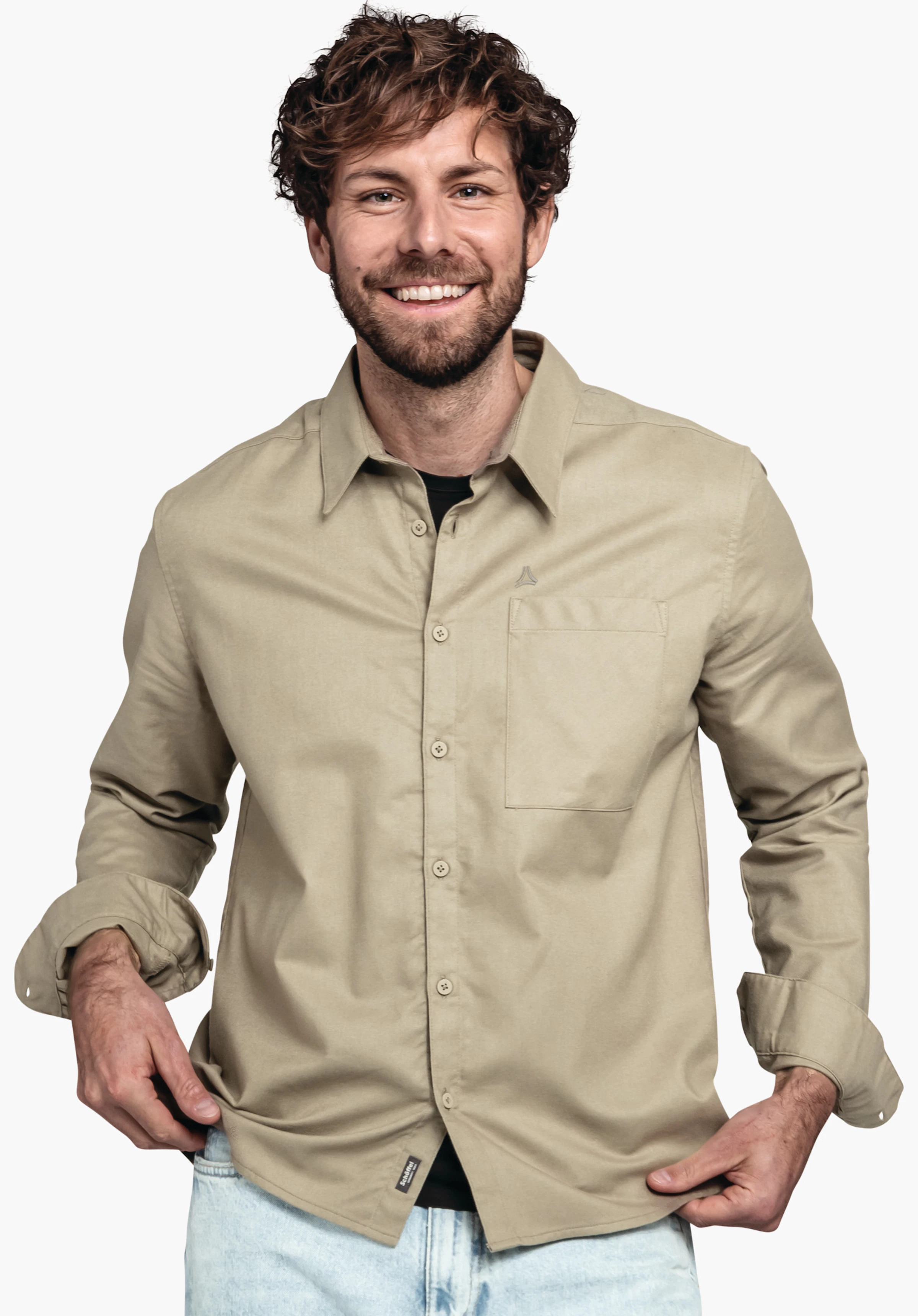 Shirt Style Kleion MNS Mann trägt hellgrünes Hemd mit Schöffel-Logo, lächelt und zieht Hemdzipfel; darunter schwarzes T-Shirt, hellblaue Jeans, stehend vor weißem Hintergrund.