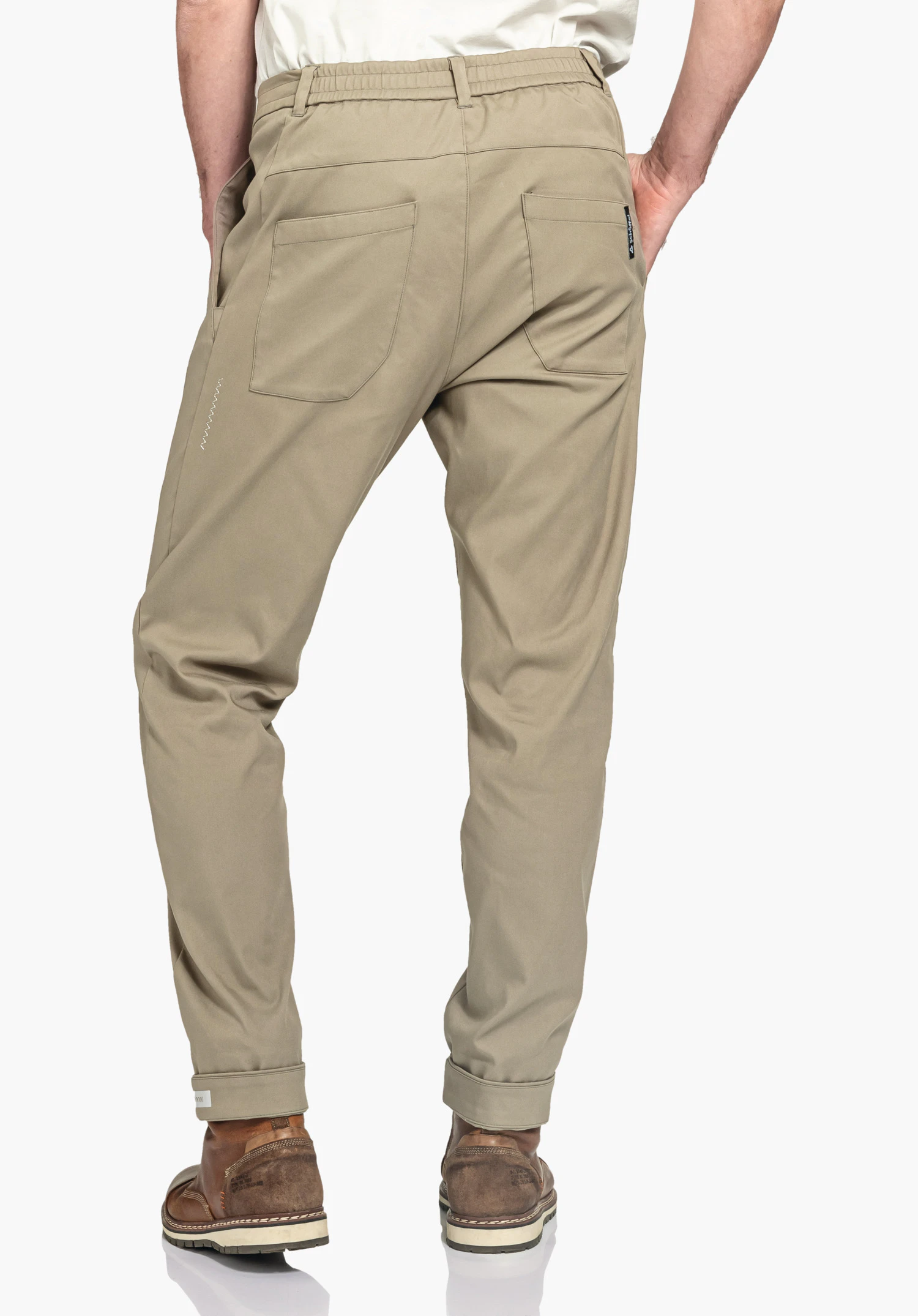 Pants Style Zourga MNS pantalon décontracté brun clair, porté de dos; personne debout avec les mains dans les poches arrière, ourlets retroussés, chaussures brun foncé et haut blanc devant un fond blanc.