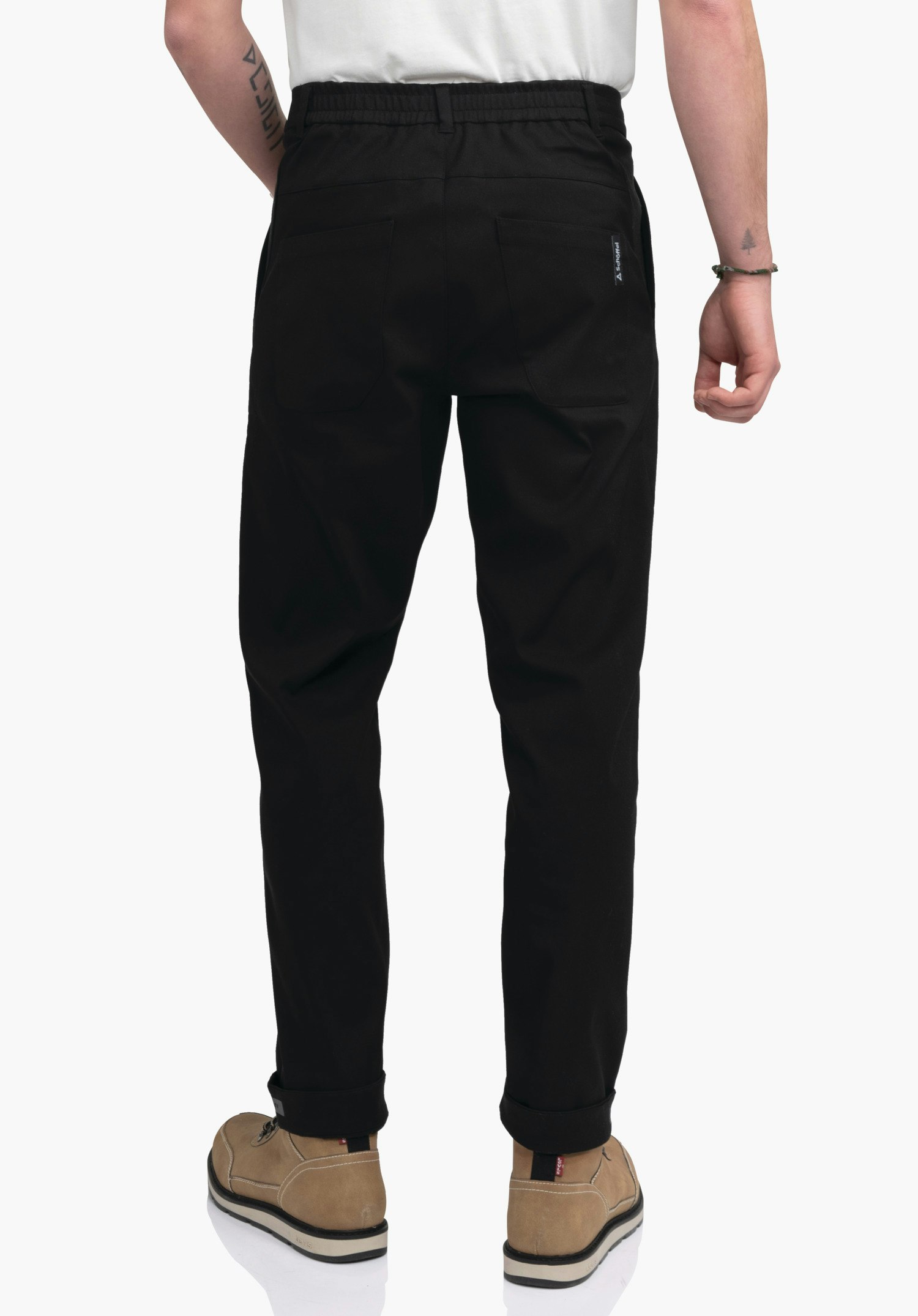 Pants Style Zourga MNS schwarze Hose zeigt Rückenansicht, sitzt locker, steht vor weißem Hintergrund; hellbraune Schuhe und weißes Shirt sichtbar; mit Schöffel-Logo an der rechten Gesäßtasche.
