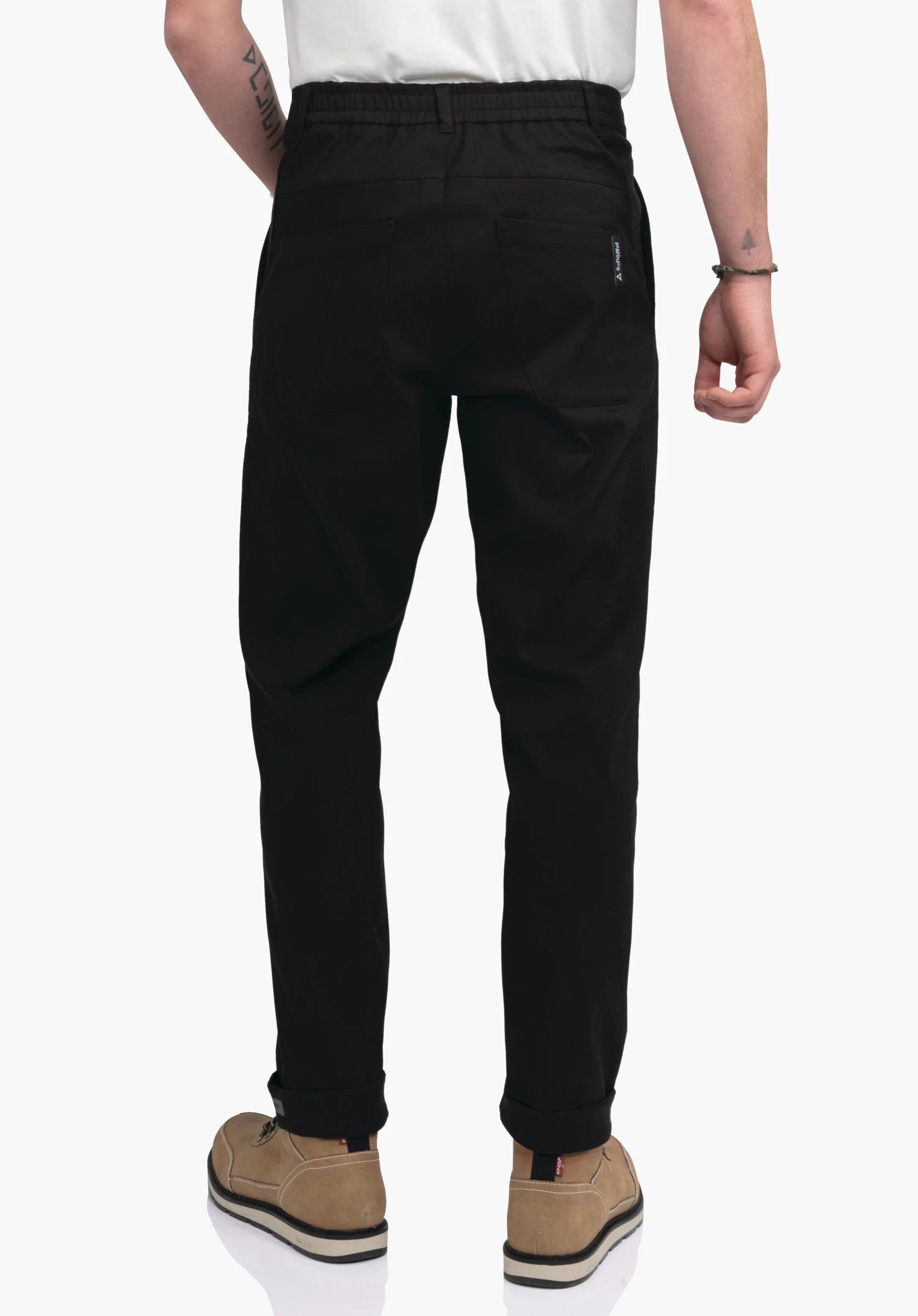 Pants Style Zourga MNS black trousers shown from the back, loose fit; standing against a white background, light brown shoes and white shirt visible; Schöffel logo on the right back pocket., Pants Style Zourga MNS black trousers shown from the back, loose fit; standing against a white background, light brown shoes and white shirt visible; Schöffel logo on the right back pocket.