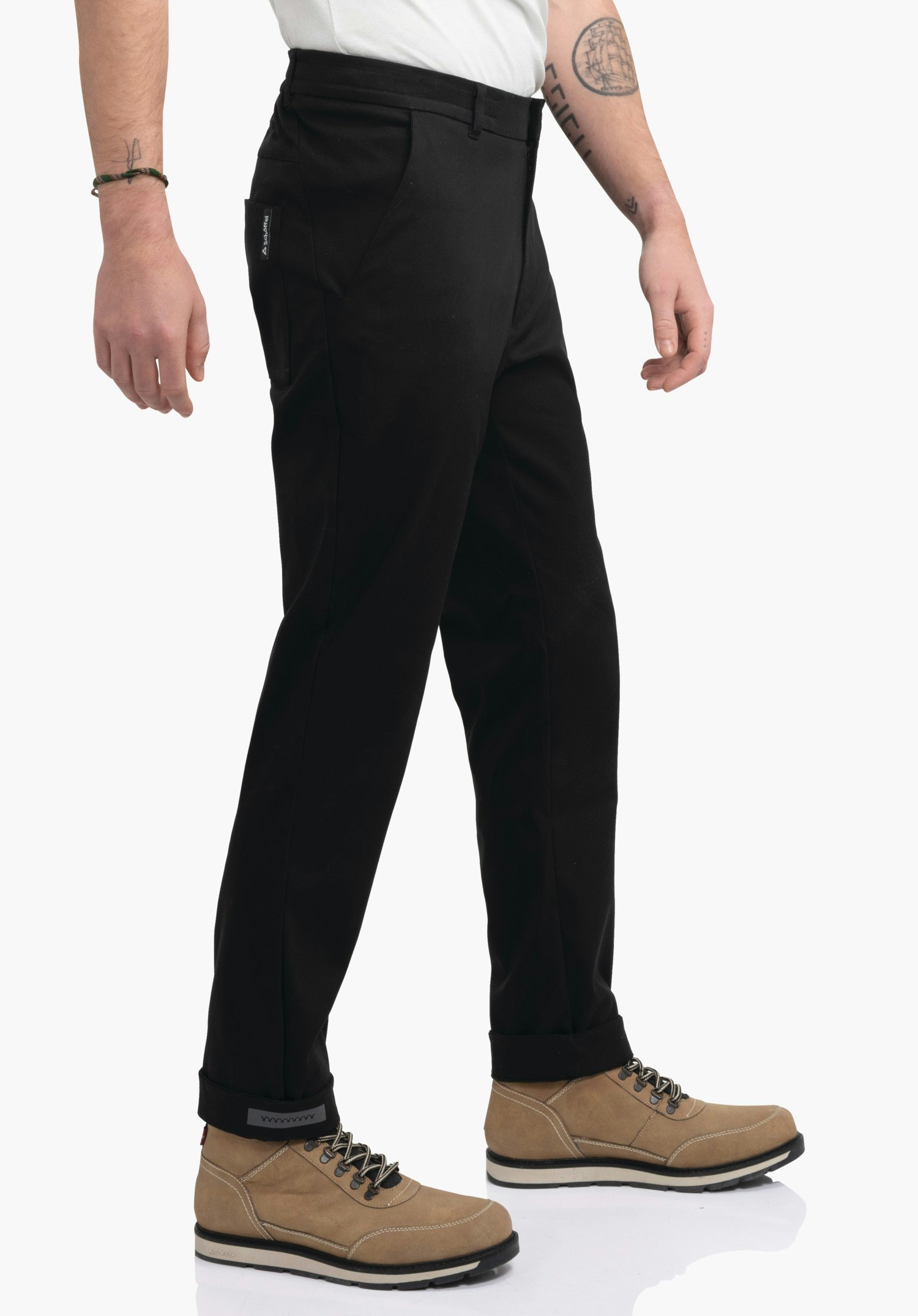 Pants Style Zourga MNS Schwarze Hose, getragen von Person, in leichter Schrittbewegung; hellbraune Stiefel, weiße Oberbekleidung, weißer Hintergrund, seitliche Tasche mit Schöffel-Logo.
