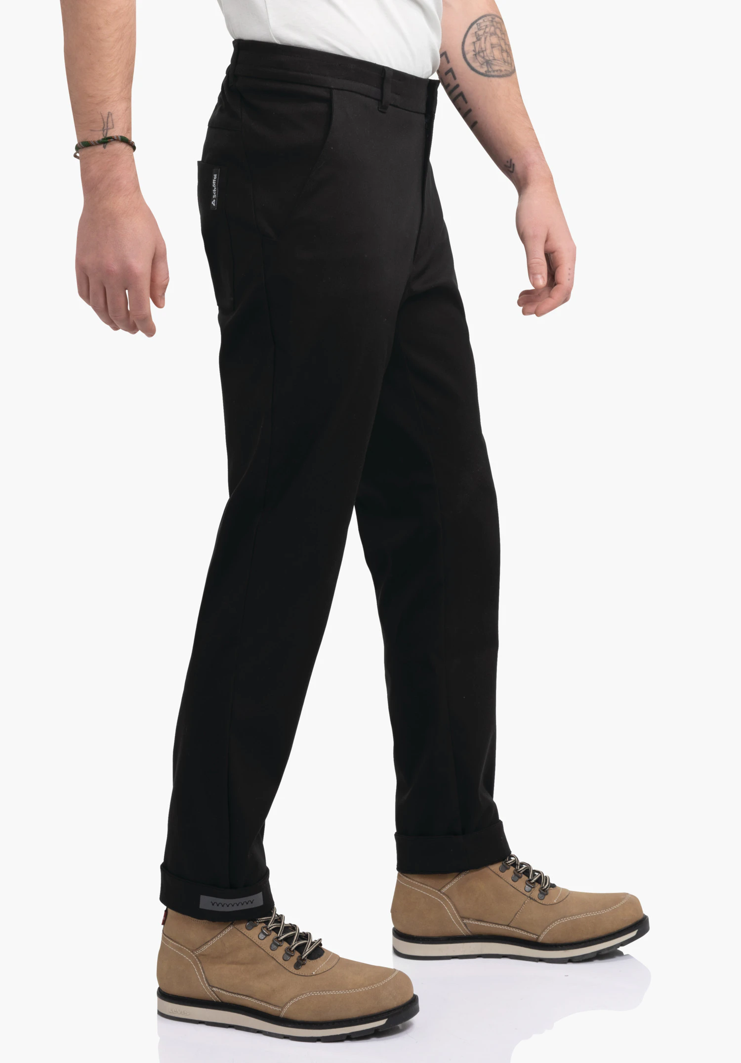 Pants Style Zourga MNS black trousers worn by a person in a light stepping motion; light brown boots, white top, white background, side pocket with Schöffel logo.