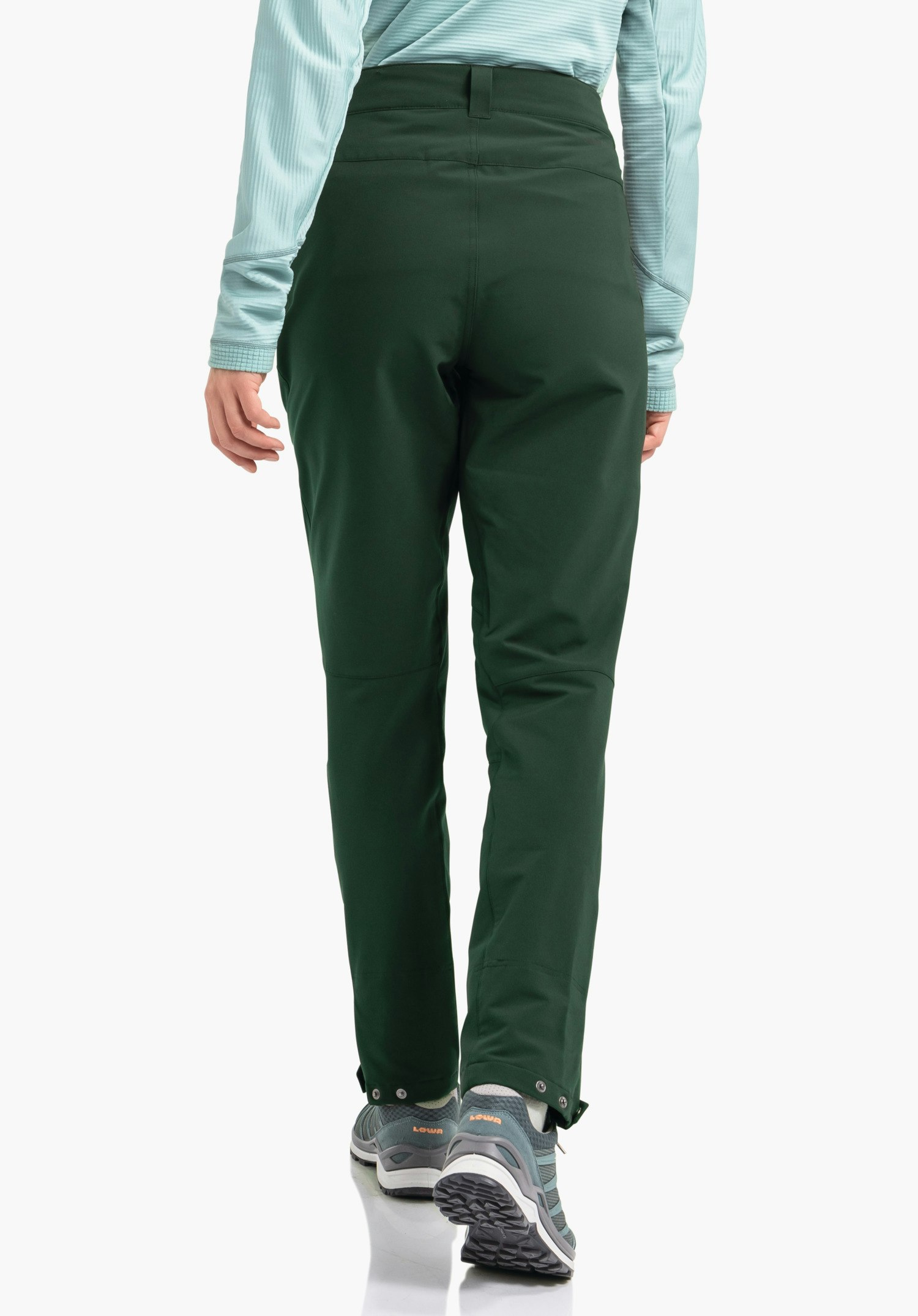 Pants Style Cascata WMS donkergroene broek, gedragen door een persoon die wegloopt; context: witte studioachtergrond, lichtblauw shirt met lange mouwen, blauwe wandelschoenen met oranje tekst "LOWA".