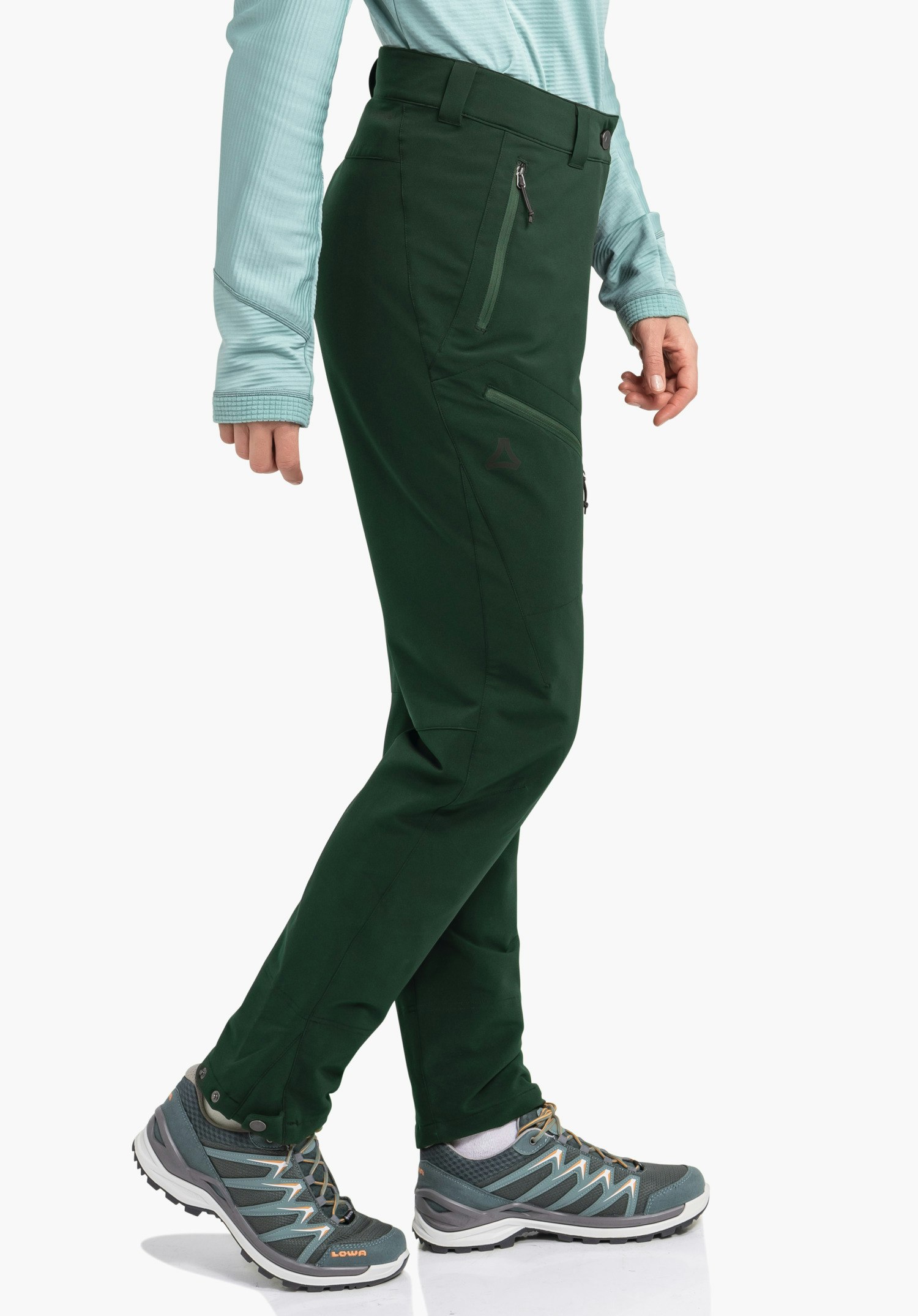 Pants Style Cascata WMS donkergroene outdoorbroek gedragen door een persoon die een stap zet; lichtblauw longsleeve shirt, grijze wandelschoenen met tekst "LOWA", Schöffel-logo aan de zijkant, witte achtergrond.