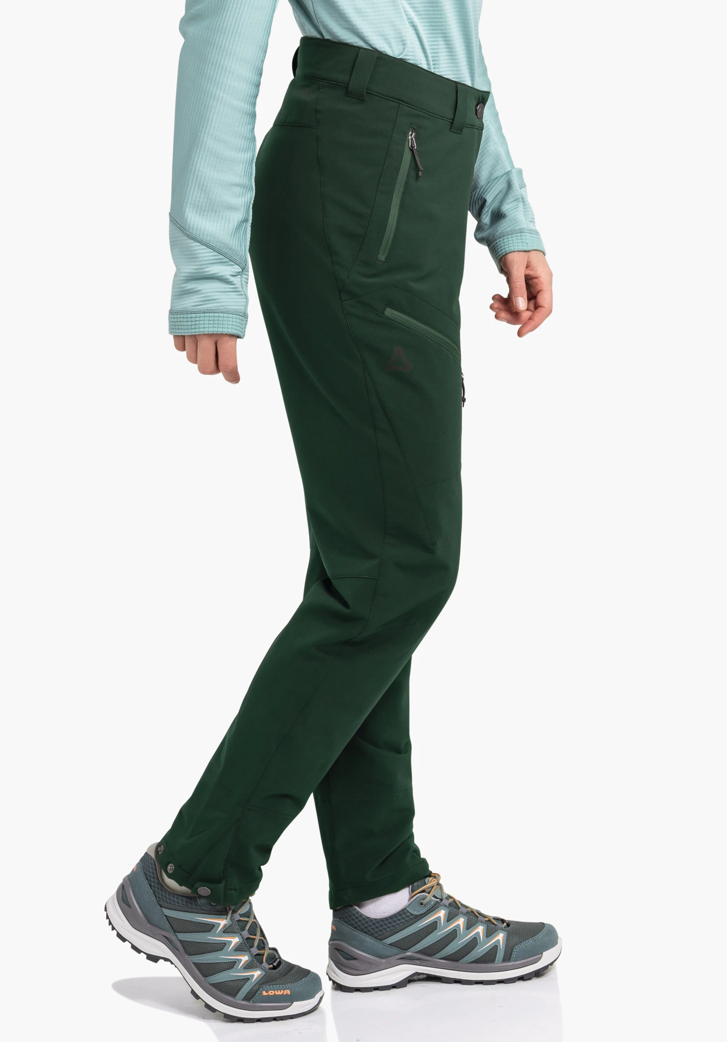 Pants Style Cascata WMS pantalon outdoor vert foncé porté par une personne faisant un pas; t-shirt manches longues bleu clair, chaussures de randonnée grises avec inscription "LOWA", logo Schöffel sur le côté, fond blanc.