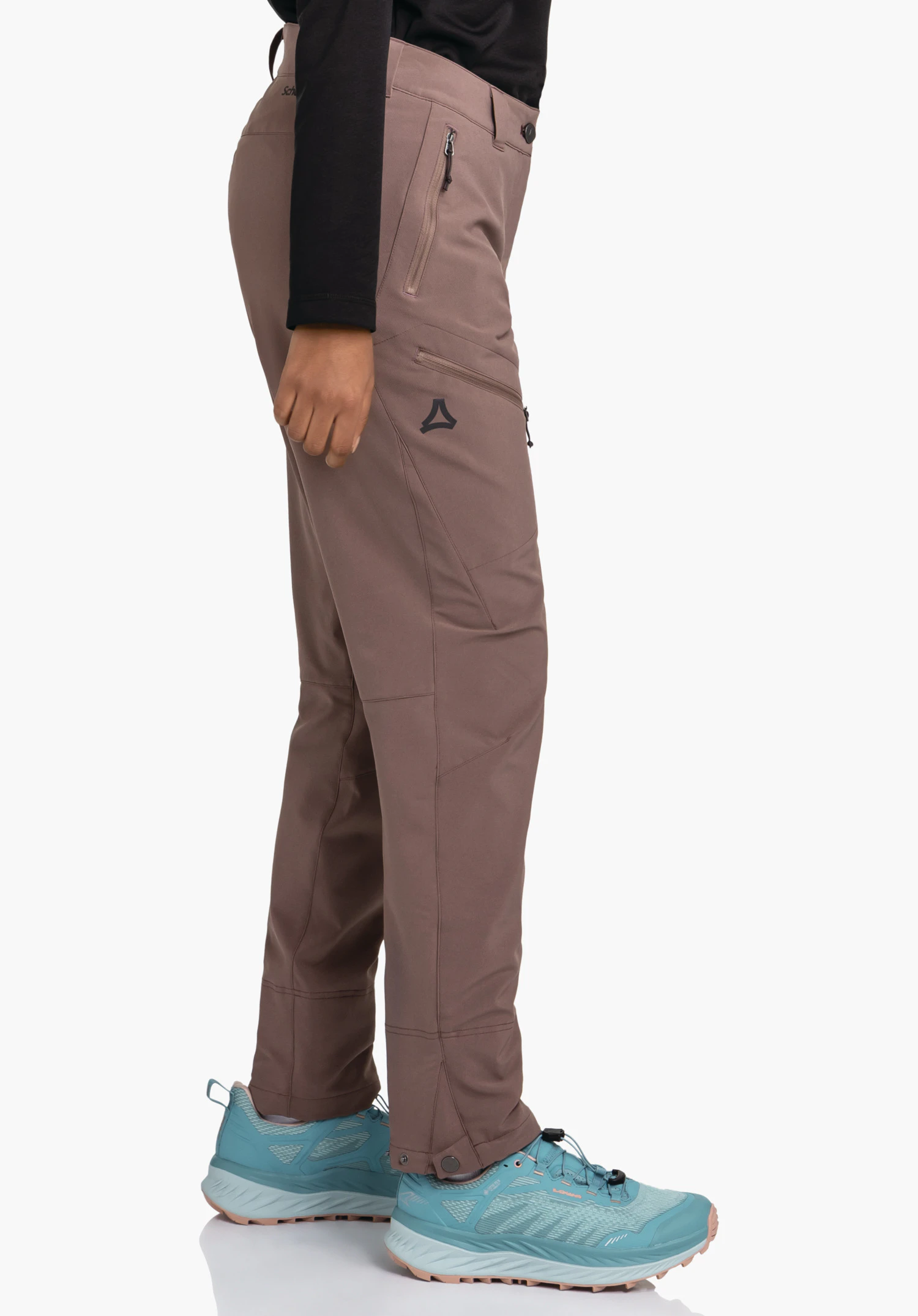 Pants Style Cascata WMS pantalon violet foncé avec logo Schöffel, porté par une personne debout; la personne porte un haut noir et des chaussures de randonnée bleu clair; fond blanc.