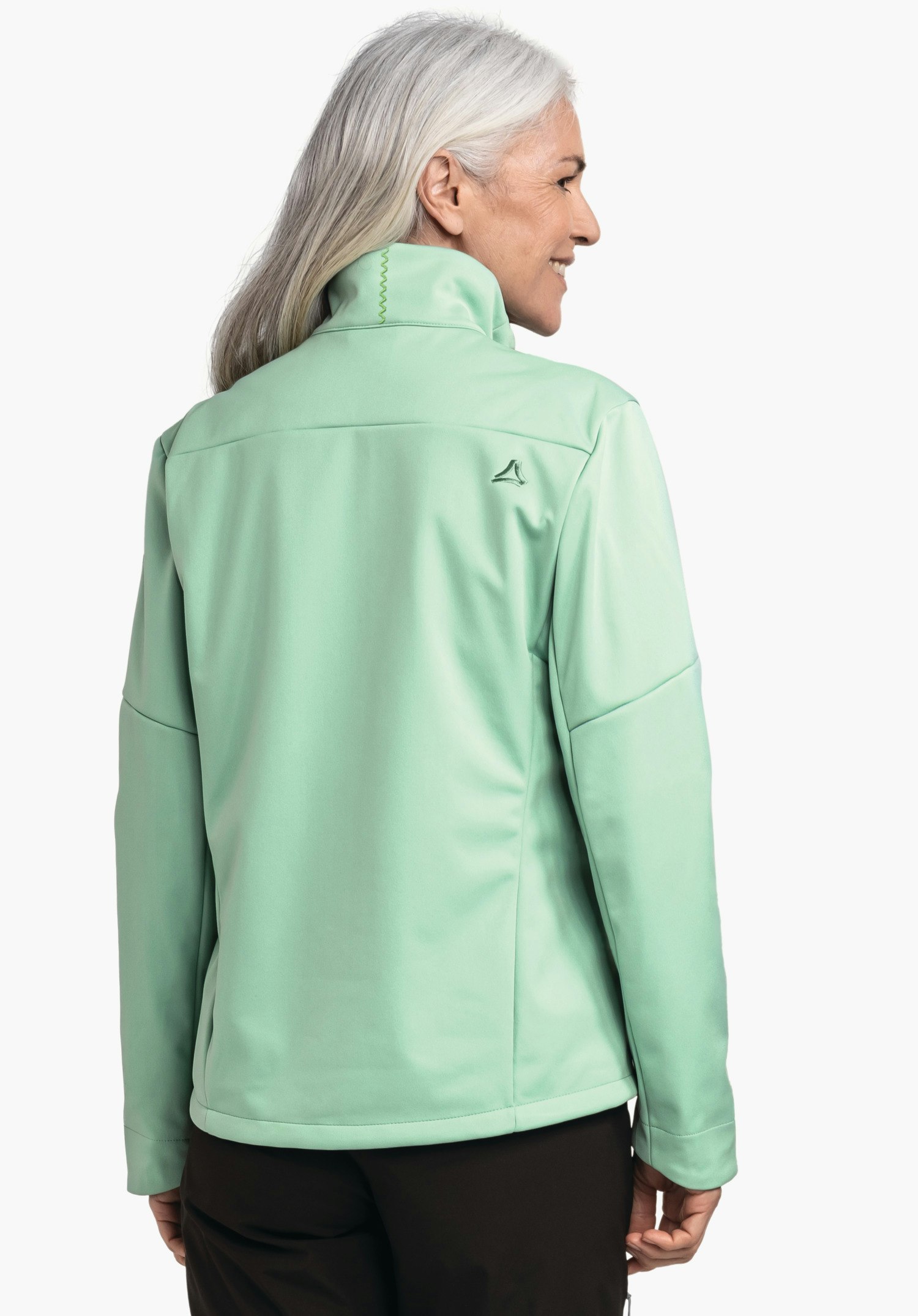 Softshell Jk Style Fracon WMS hellgrüne Jacke, getragen von einer Frau mit weißem Haar, die seitlich lächelt; Schöffel-Logo dunkelgrün auf dem Rücken; weißer Studiohintergrund.
