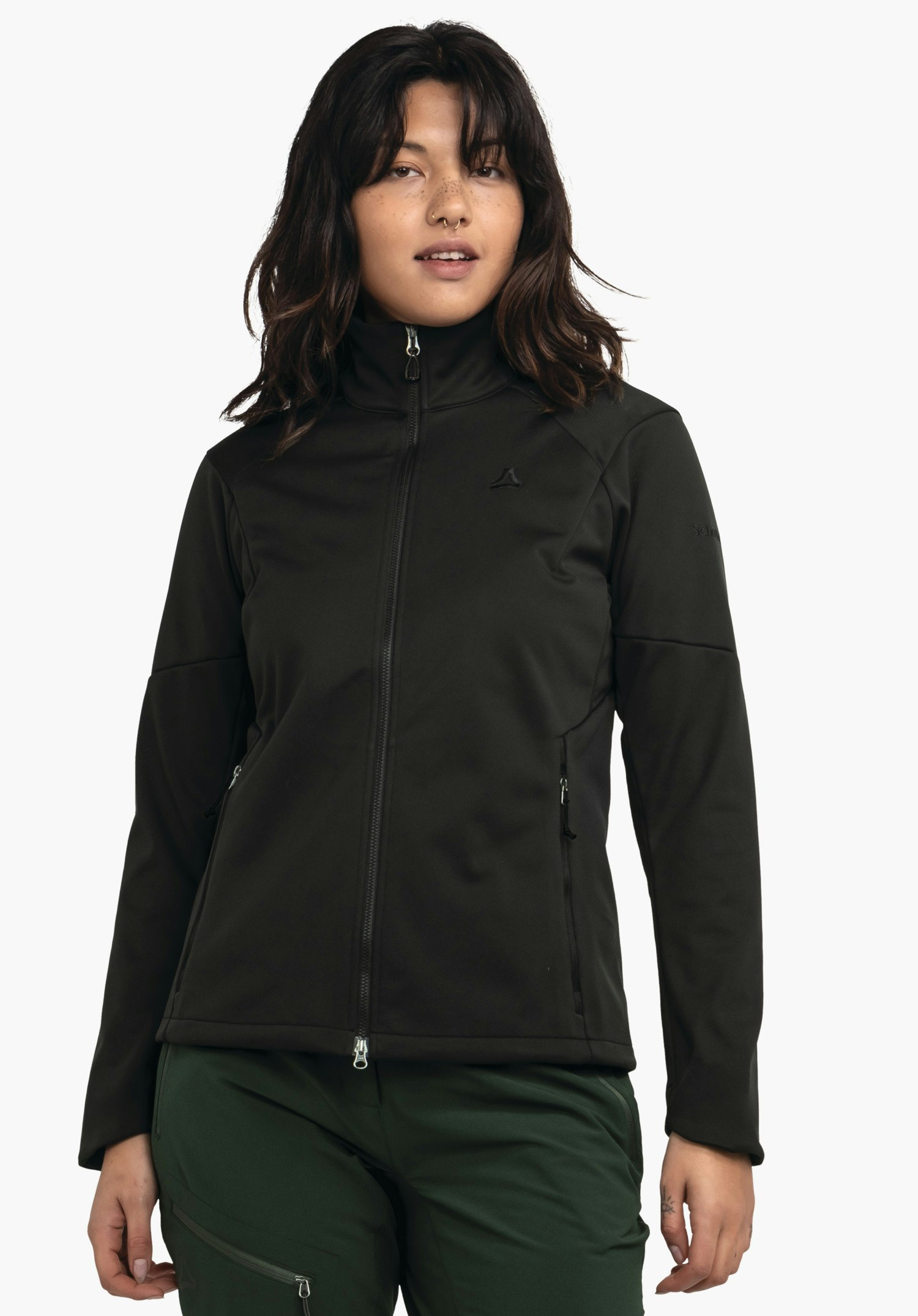 Softshell Jk Style Fracon WMS Veste noire zip fermée, portée longueur hanches par une personne debout devant un fond blanc; logo Schöffel sur la poitrine, marquage «Schöffel» sur la manche gauche; pantalon vert foncé.