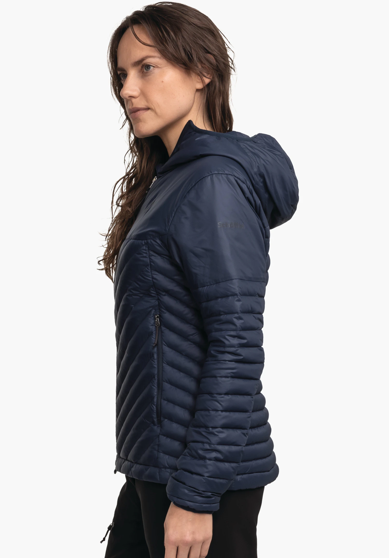 Down Jacket Style Cascata WMS donkerblauwe gewatteerde jas, zijwaarts gedragen door een vrouw die stil staat, capuchon op de rug; zichtbare ritszak; neutrale witte achtergrond. Tekst op de mouw: "Schöffel".