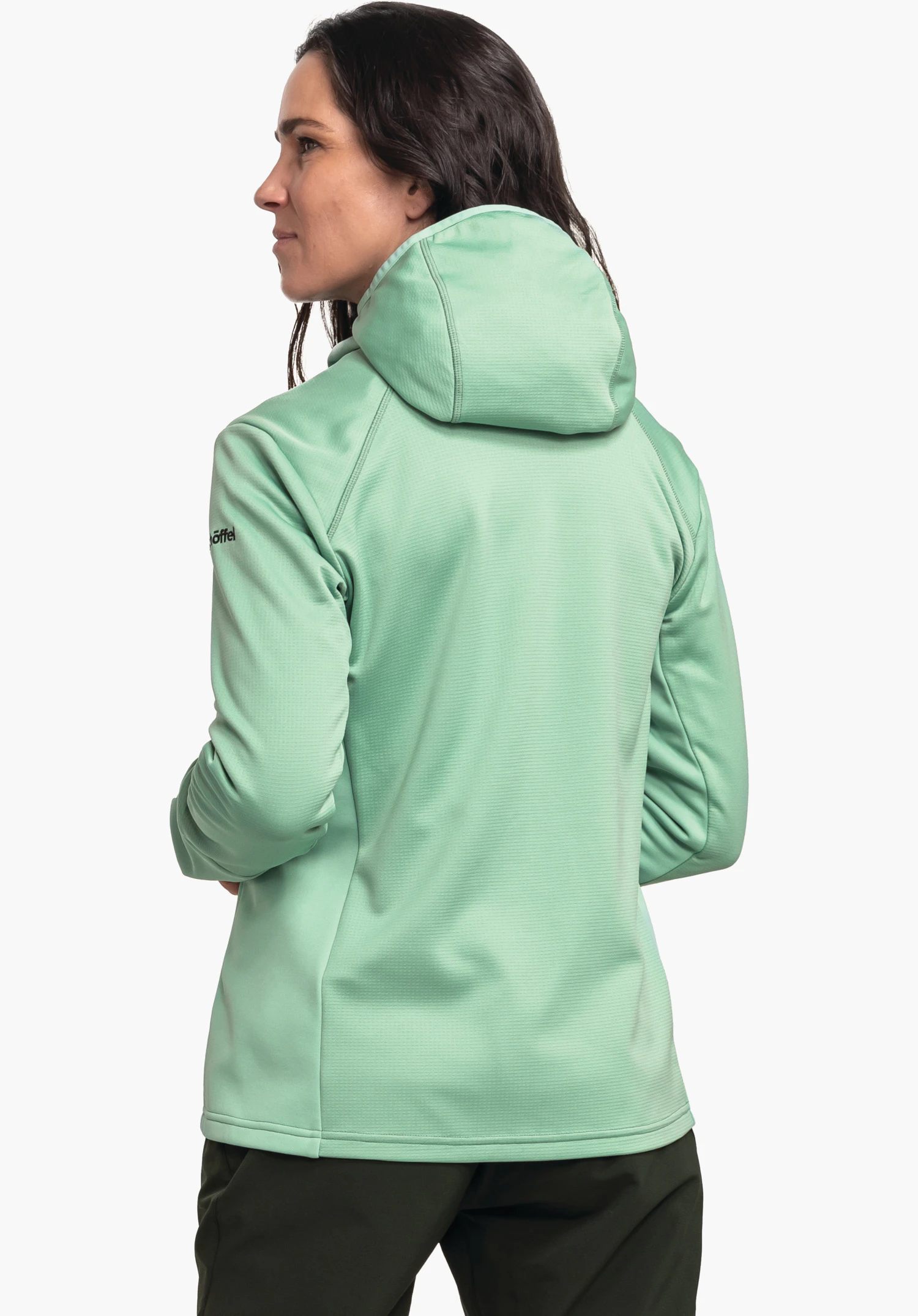 Fleece Hoody Style Milagle WMS veste à capuche vert clair, portée par une femme debout regardant vers la gauche; mains sur les hanches; pantalon vert foncé devant un fond blanc. Texte sur la manche: « Schöffel ».
