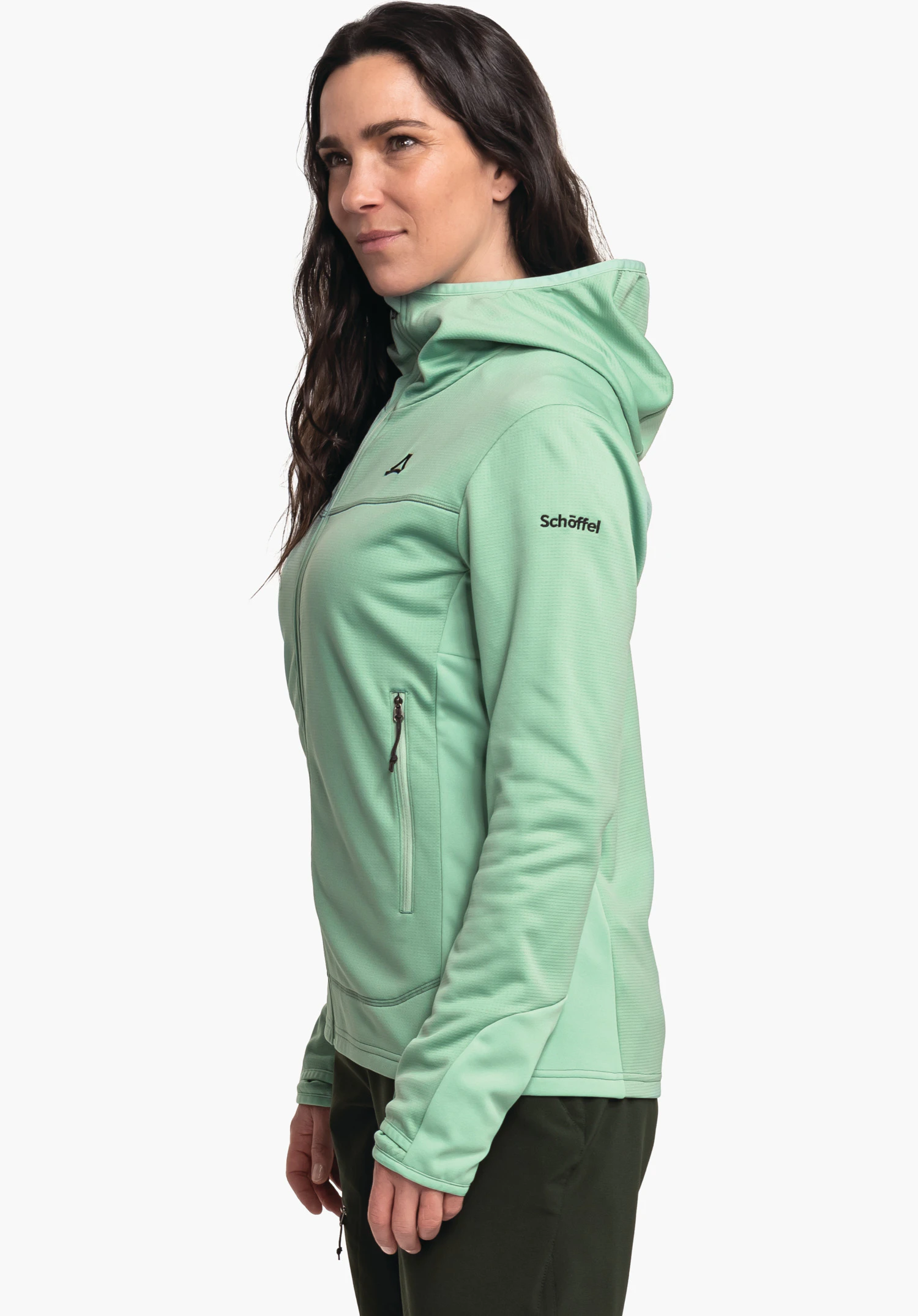 Fleece Hoody Style Milagle WMS femme portant une veste à capuche vert clair, debout de profil, regard vers l’avant; veste avec logo Schöffel sur la poitrine et texte "Schöffel" sur la manche; contexte: fond blanc, pantalon vert foncé.
