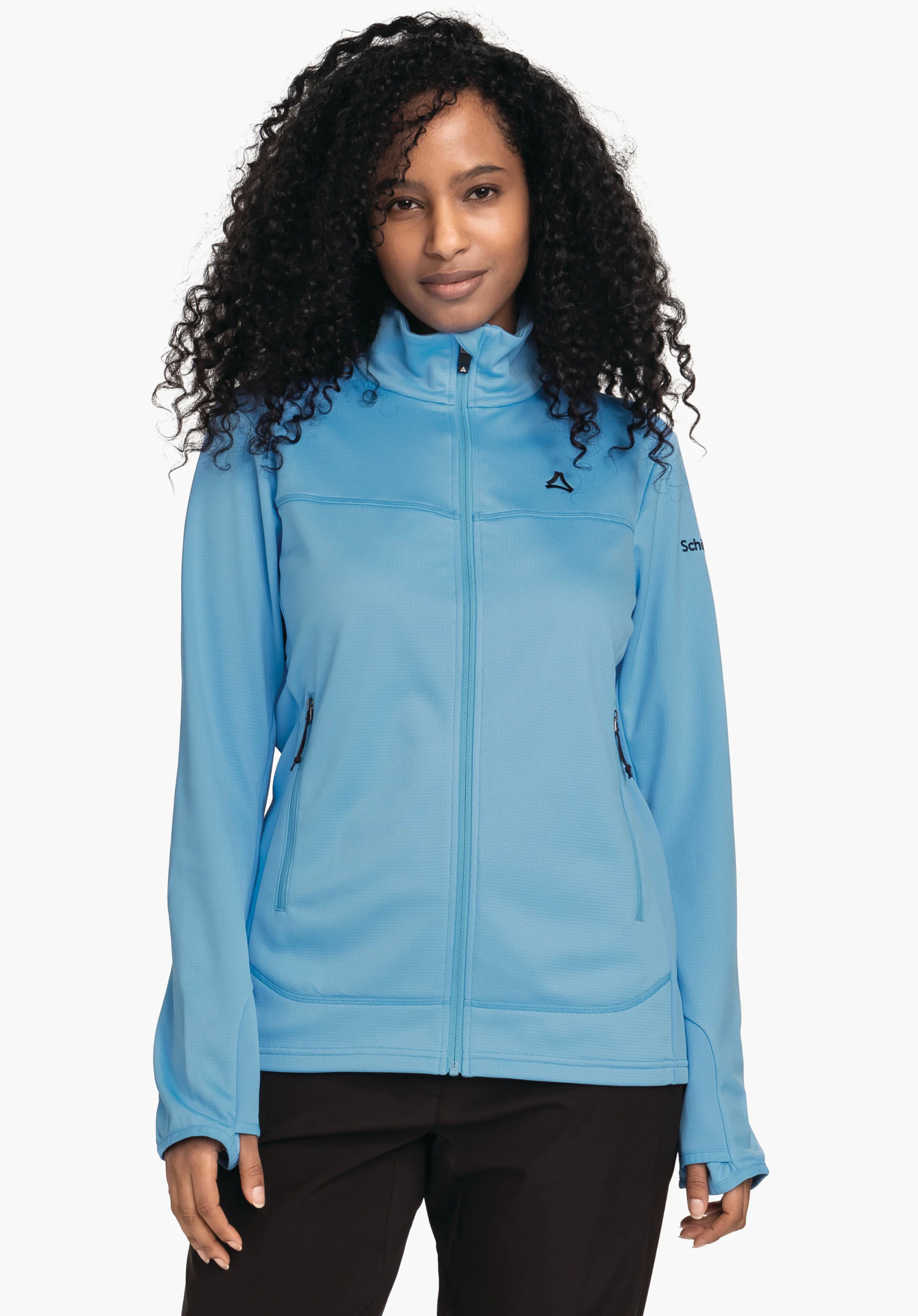 Fleece Jk Style Milagle WMS Veste softshell bleu clair portée de face par une personne; logo Schöffel sur la poitrine, marquage «Schöffel» sur la manche; cheveux noirs bouclés, fond blanc, pantalon noir.