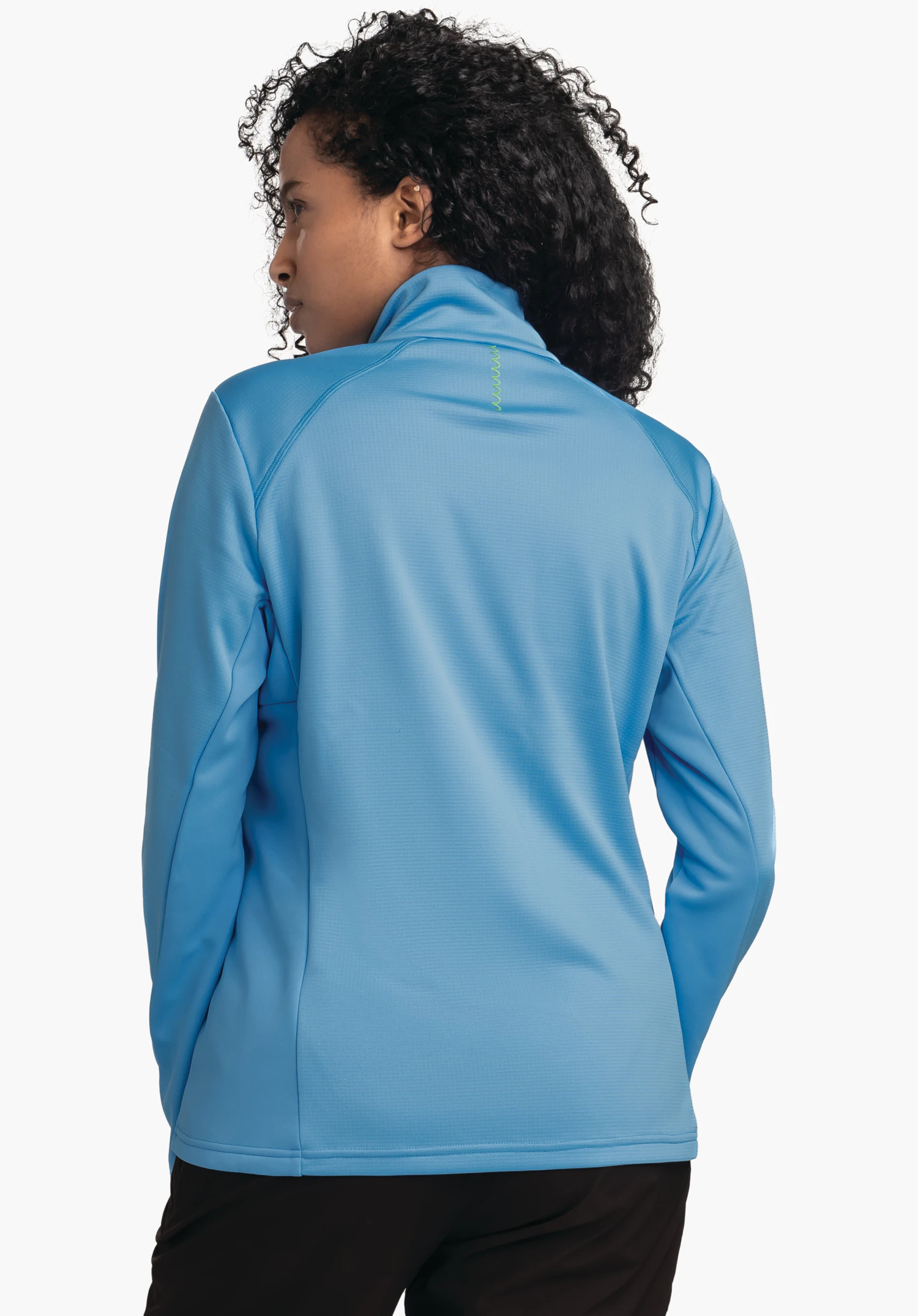 Fleece Jk Style Milagle WMS veste bleu clair, portée par une femme vue de dos, tête tournée vers la gauche; cheveux noirs bouclés, pantalon noir; fond studio blanc.
