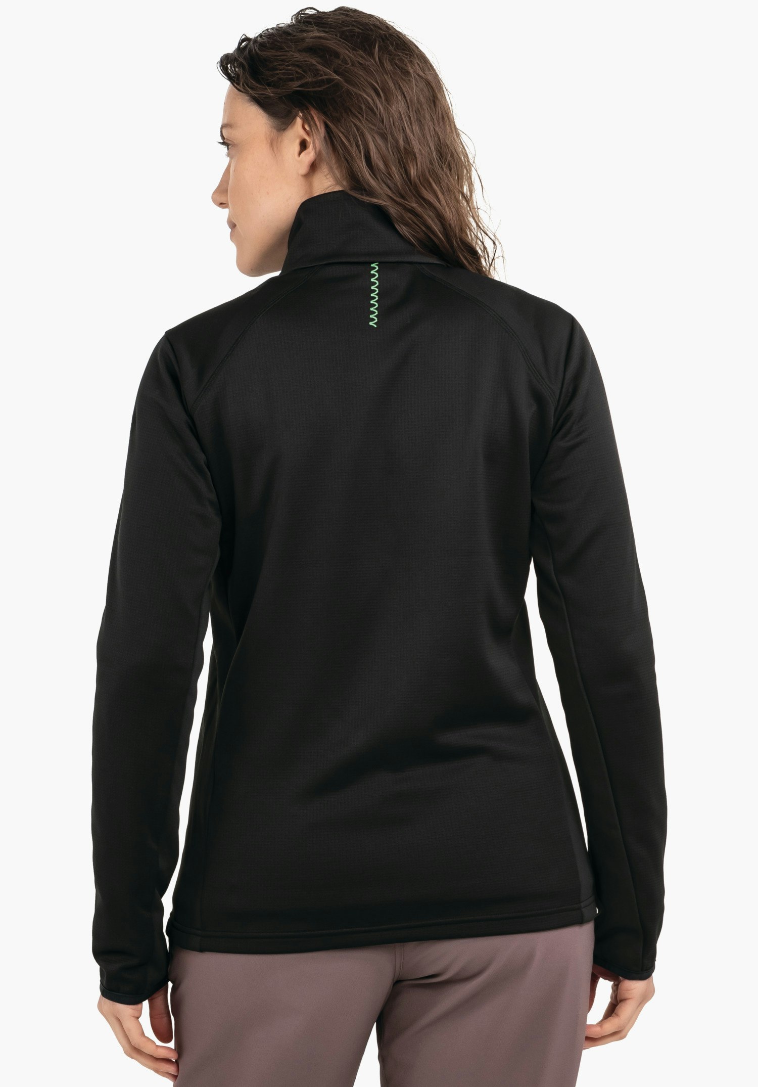Fleece Jk Style Milagle WMS veste noire, vue arrière: femme debout regardant vers la gauche; cheveux brun clair, pantalon rose foncé, fond studio blanc, couture décorative verte en zigzag sur le haut du dos.