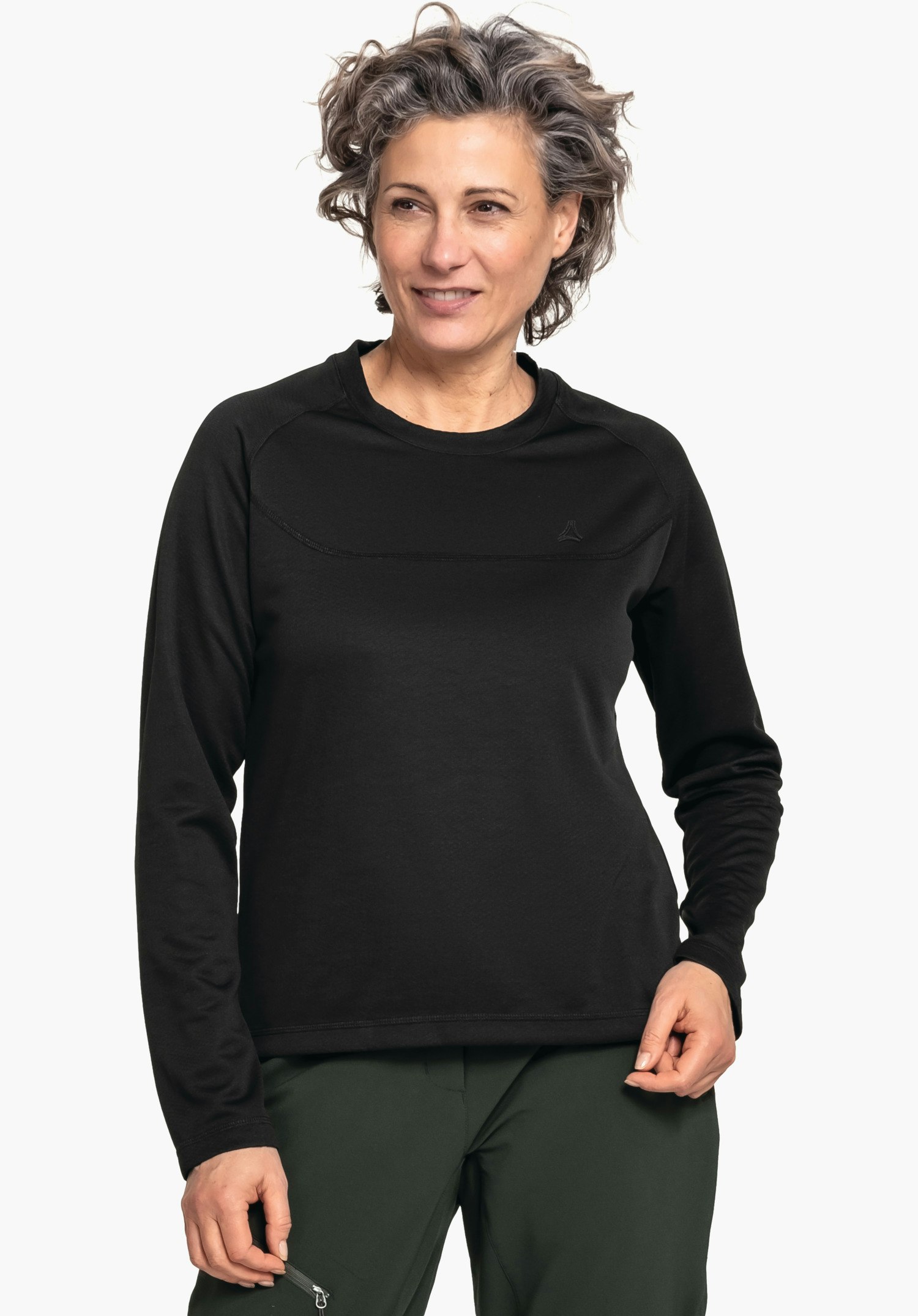 CIRC Longsleeve Smue WMS Haut manches longues noir porté par une femme souriante regardant légèrement de côté; logo Schöffel sur la poitrine; debout devant un fond neutre, pantalon vert foncé visible.