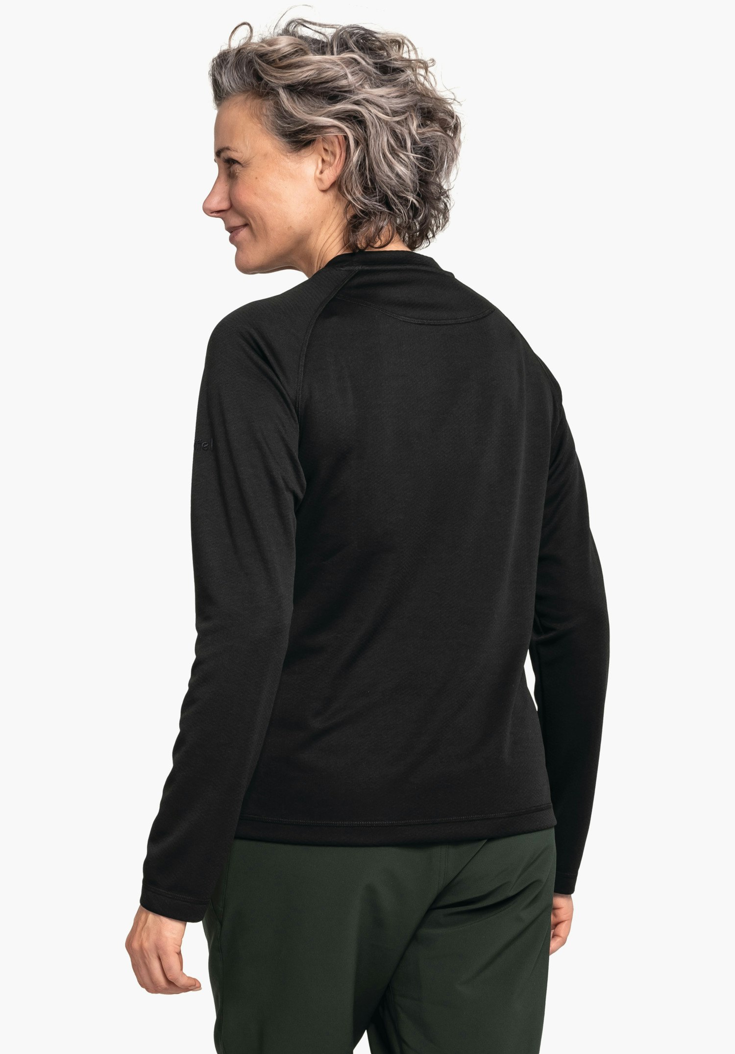 CIRC Longsleeve Smue WMS Frau in schwarzem Langarmshirt steht, schaut über die Schulter nach links; trägt dunkelgrüne Hosen; heller, neutraler Studiohintergrund.