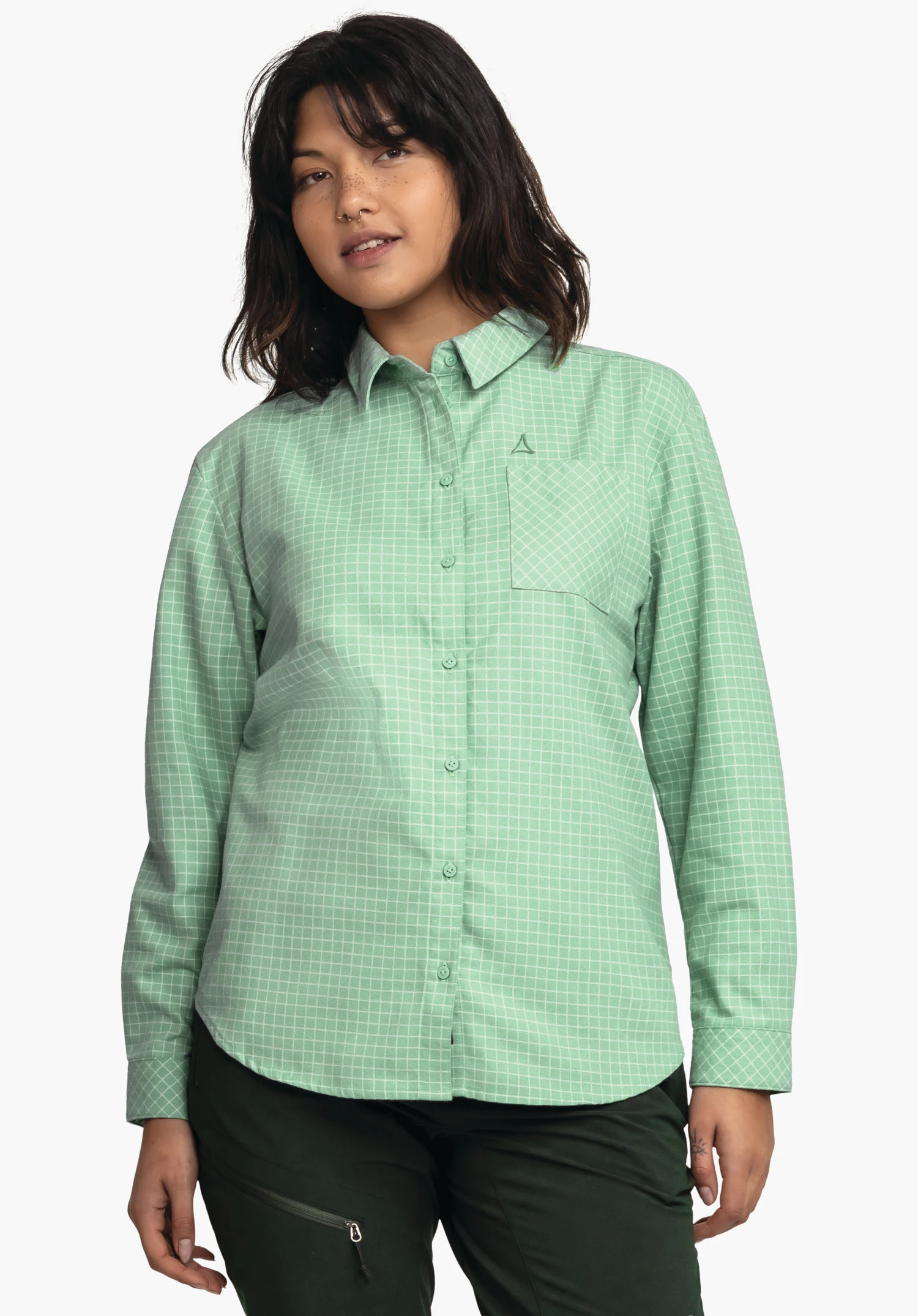 Blouse Style Boyoma WMS Chemise manches longues à carreaux vert clair et blanc portée par une femme; avec poche poitrine et logo Schöffel, associée à un pantalon vert foncé; fond clair.