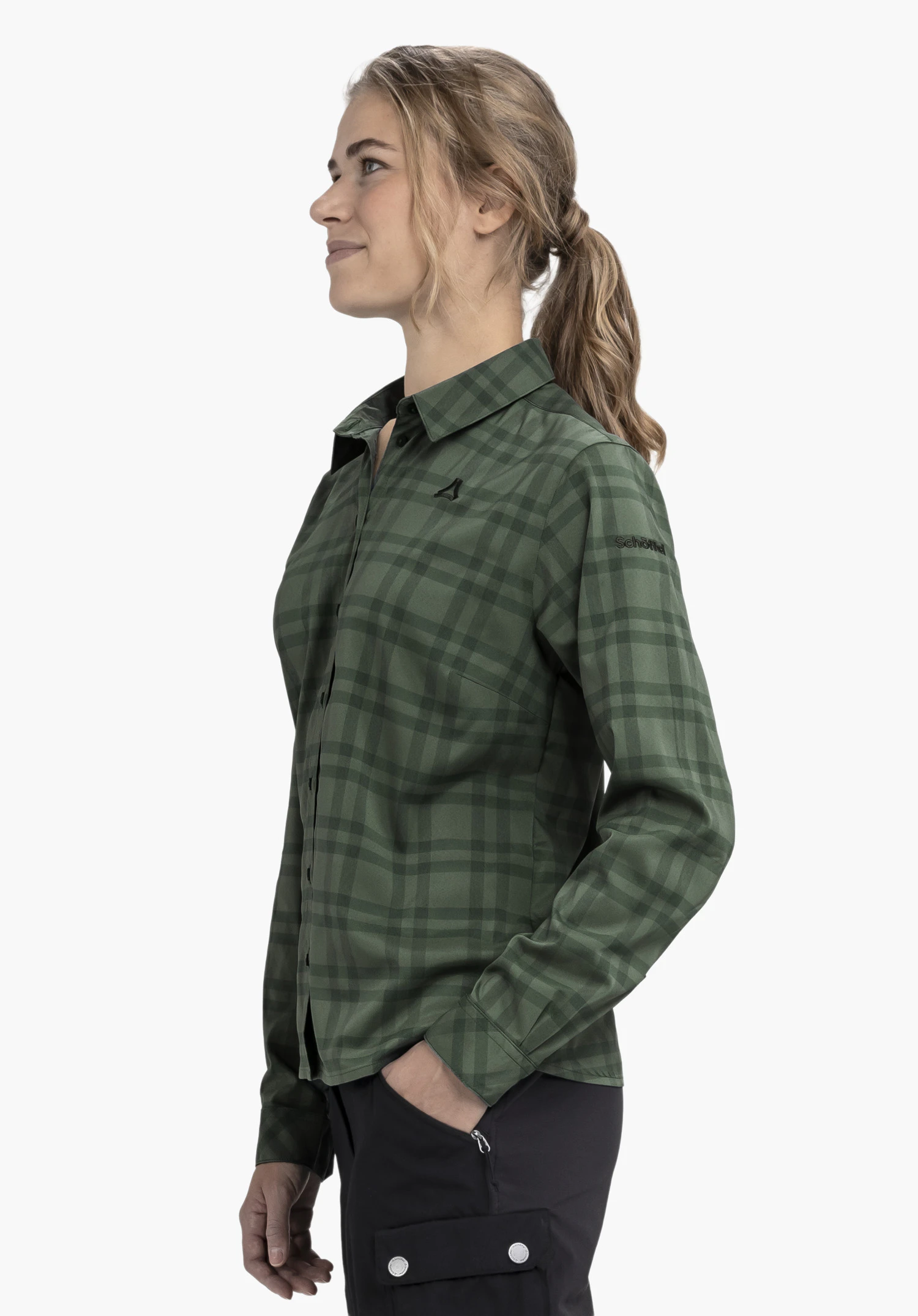 Blouse Style Yekuro WMS chemise manches longues à carreaux vert foncé; logo Schöffel sur la poitrine, inscription "Schöffel" sur la manche; personne en profil, regard vers la gauche, mains dans les poches, fond blanc.