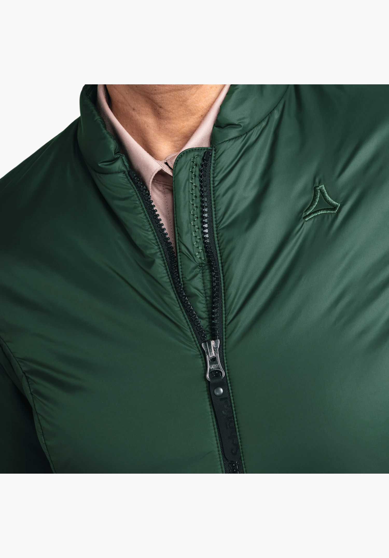 Ins Jacket Style Malkay WMS montrant le col, la fermeture éclair et le logo Schöffel brodé sur le tissu vert en gros plan sur fond blanc/neutre.
