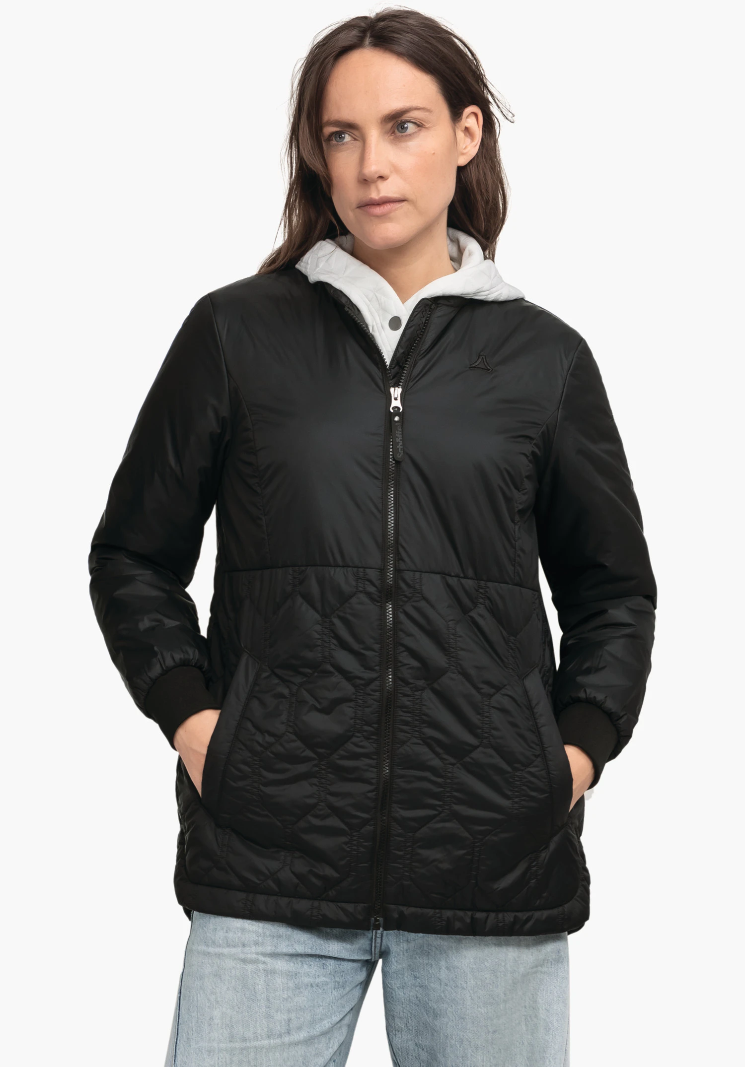 Ins Jacket Style Malkay WMS black quilted jacket worn by a woman standing with hands in pockets and looking to the right; white hood visible, light blue jeans; neutral background; Schöffel logo on the chest.