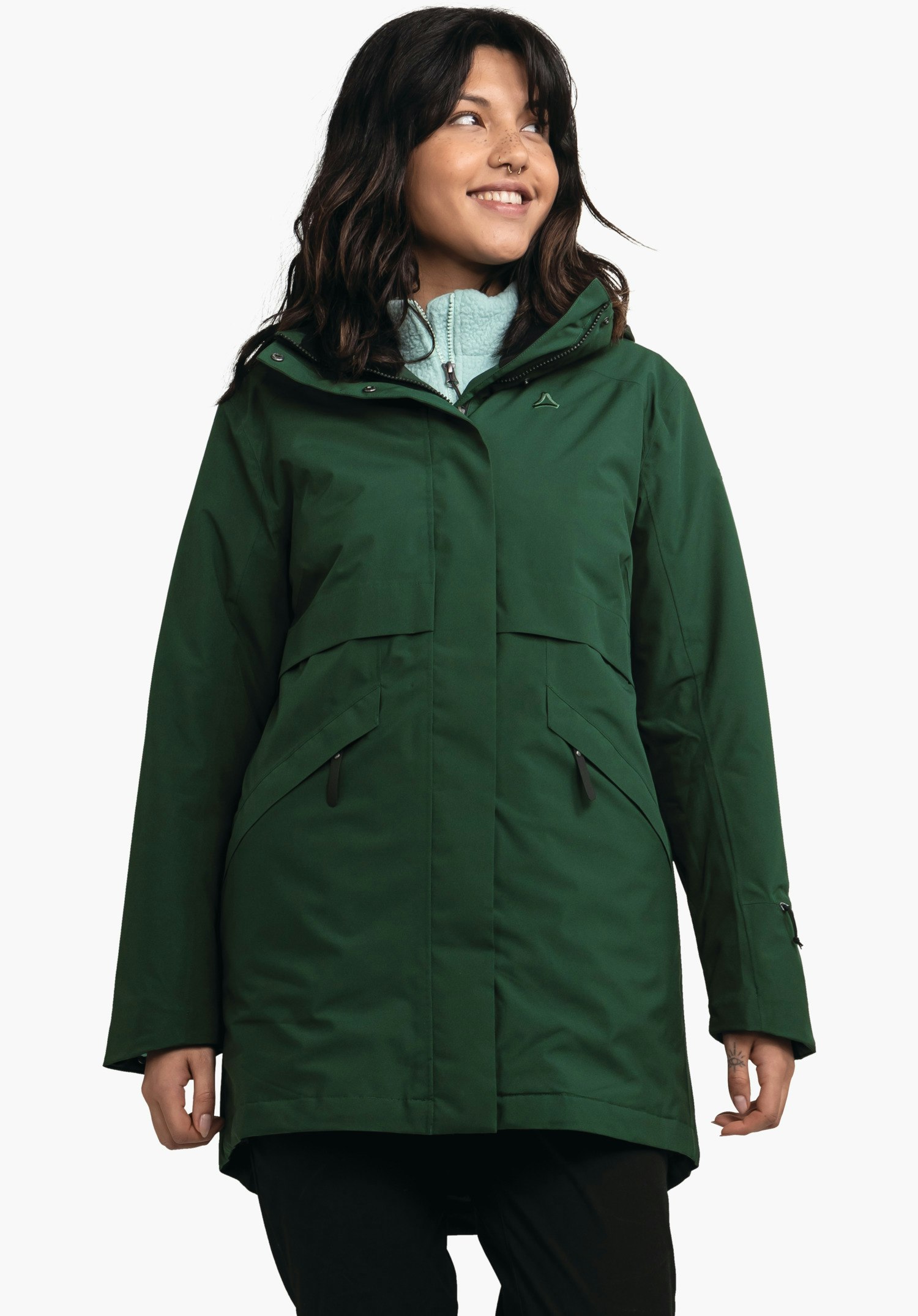 Ins Parka Style Malkay WMS Parka vert foncé portée par une personne debout souriante regardant de côté; polaire bleu clair visible en dessous, logo Schöffel sur la poitrine; fond studio blanc.