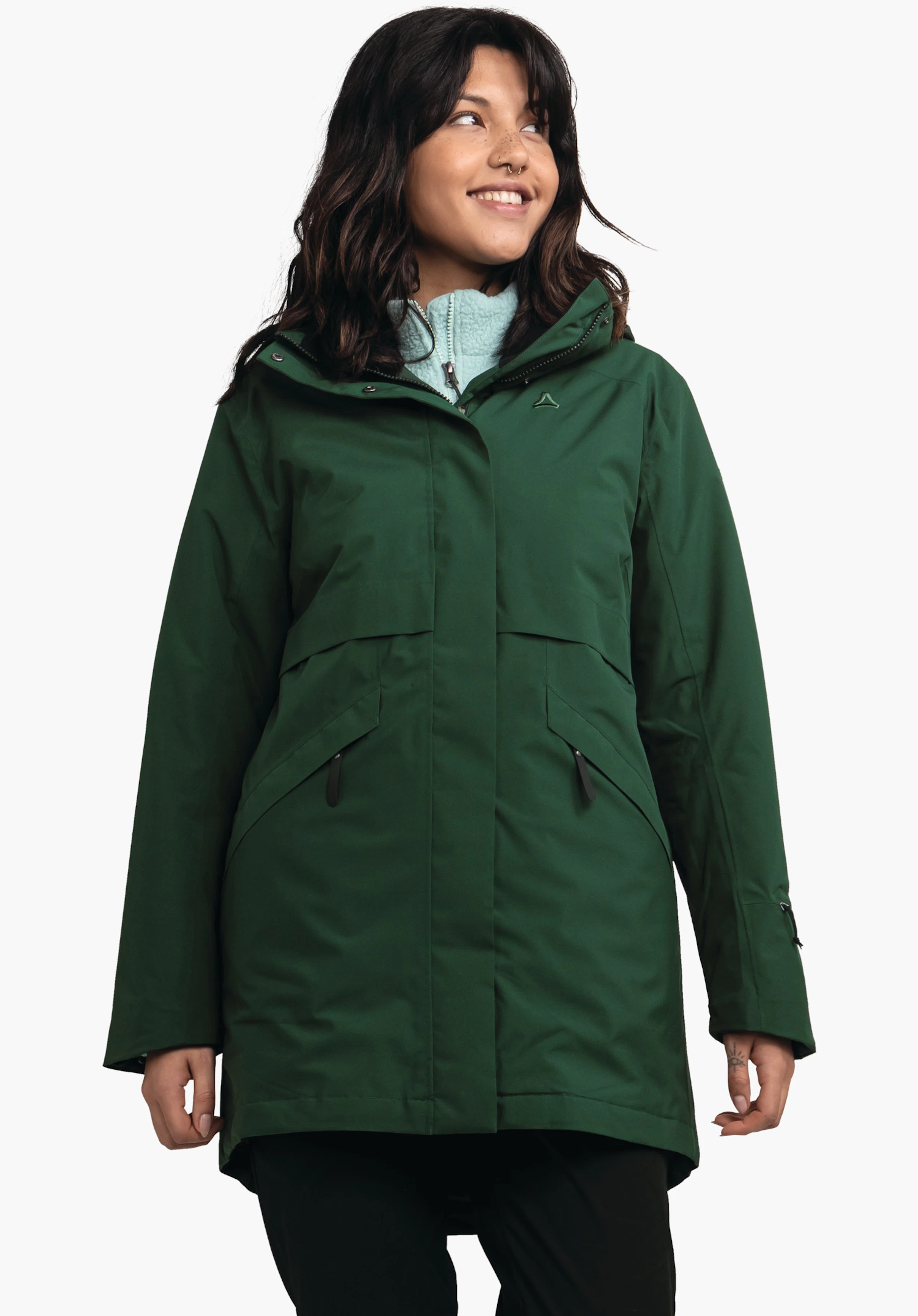 Ins Parka Style Malkay WMS dunkelgrüne Parka-Jacke, getragen von stehender Person, lächelnd und zur Seite blickend; hellblaues Fleece sichtbar, Schöffel-Logo auf der Brust, weißer Studiohintergrund.