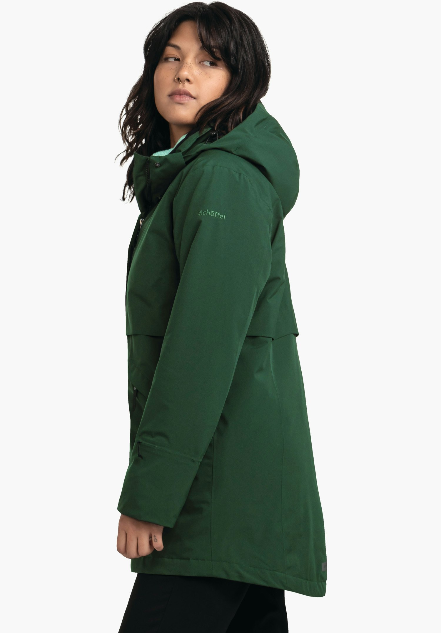 Ins Parka Style Malkay WMS parka vert foncé porté par une personne regardant de profil vers la gauche; capuche relevée; manche avec inscription "schöffel"; fond blanc clair neutre.