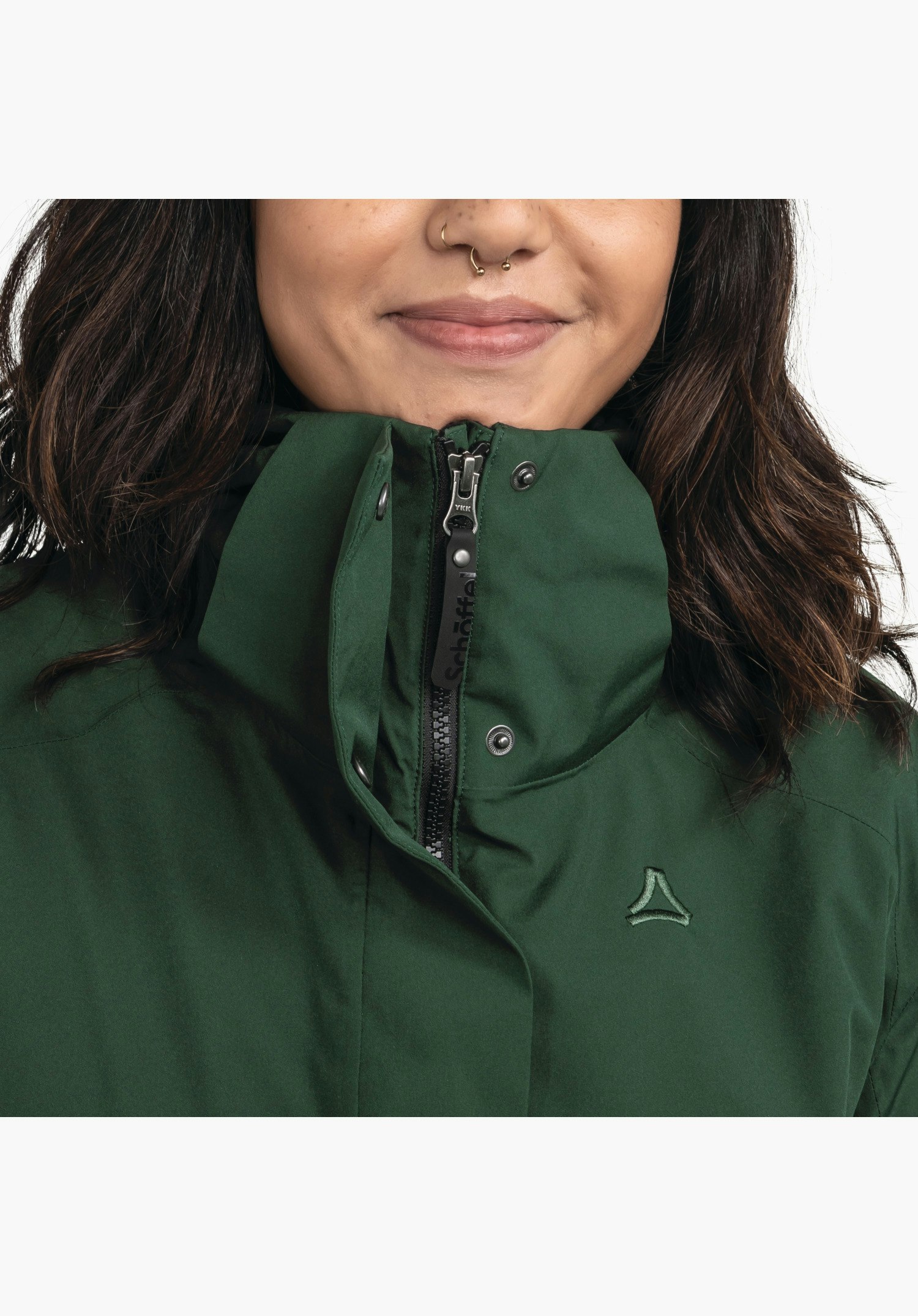 Ins Parka Style Malkay WMS présente le col haut avec fermeture éclair, la tirette de marque et le logo Schöffel brodé sur la poitrine verte. Gros plan sur fond blanc/neutre.