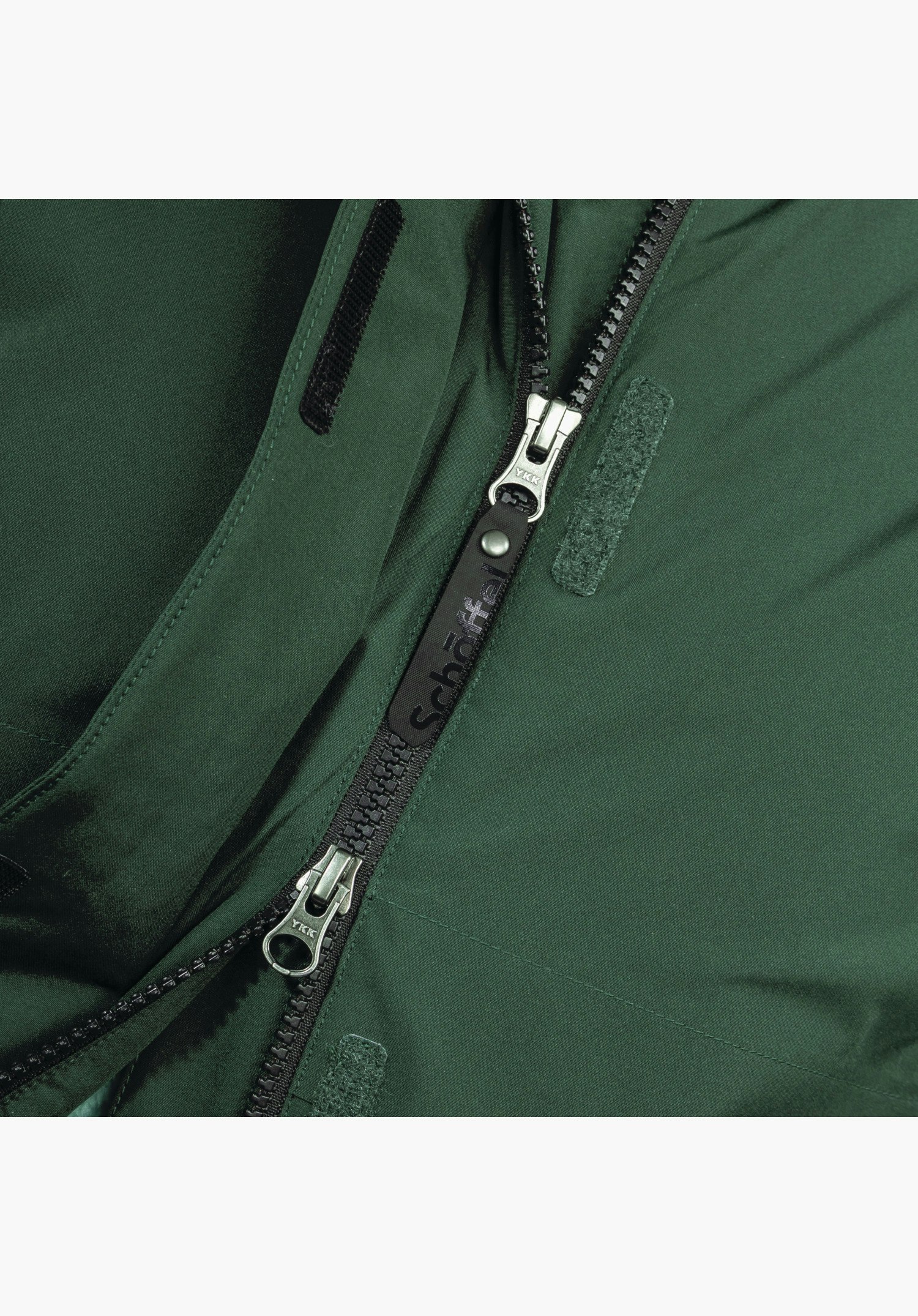 Ins Parka Style Malkay WMS montre la fermeture éclair bidirectionnelle noire avec une tirette arborant le logo Schöffel et des fermetures velcro sur le tissu vert en gros plan sur fond blanc.