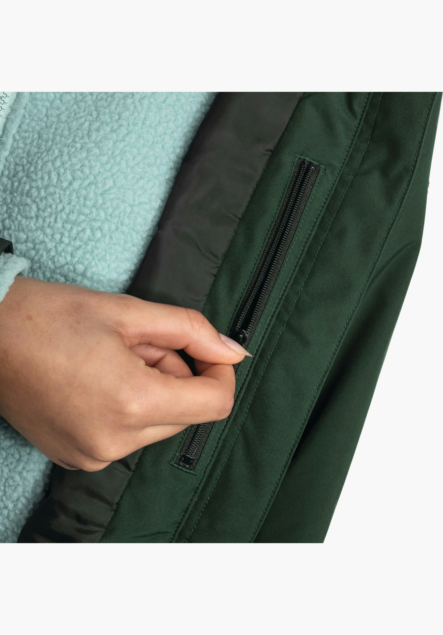 Ins Parka Style Malkay WMS montrant l'intérieur avec une poche zippée pratique dans le tissu vert manipulée par une main, gros plan sur fond blanc.