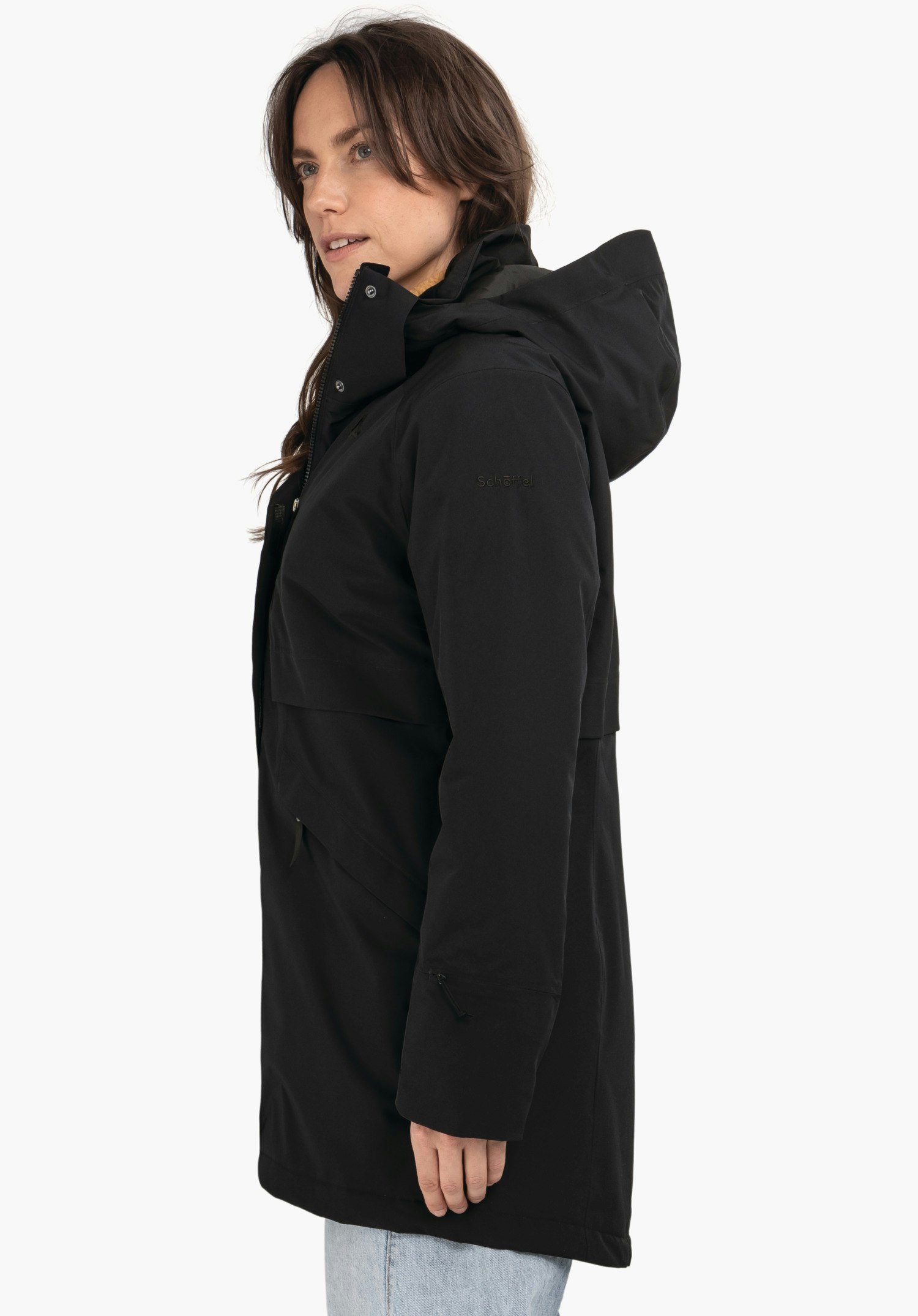 Ins Parka Style Malkay WMS femme portant une veste à capuche noire, debout de profil et regardant vers la droite; fond blanc. Texte sur la manche: "Schöffel".