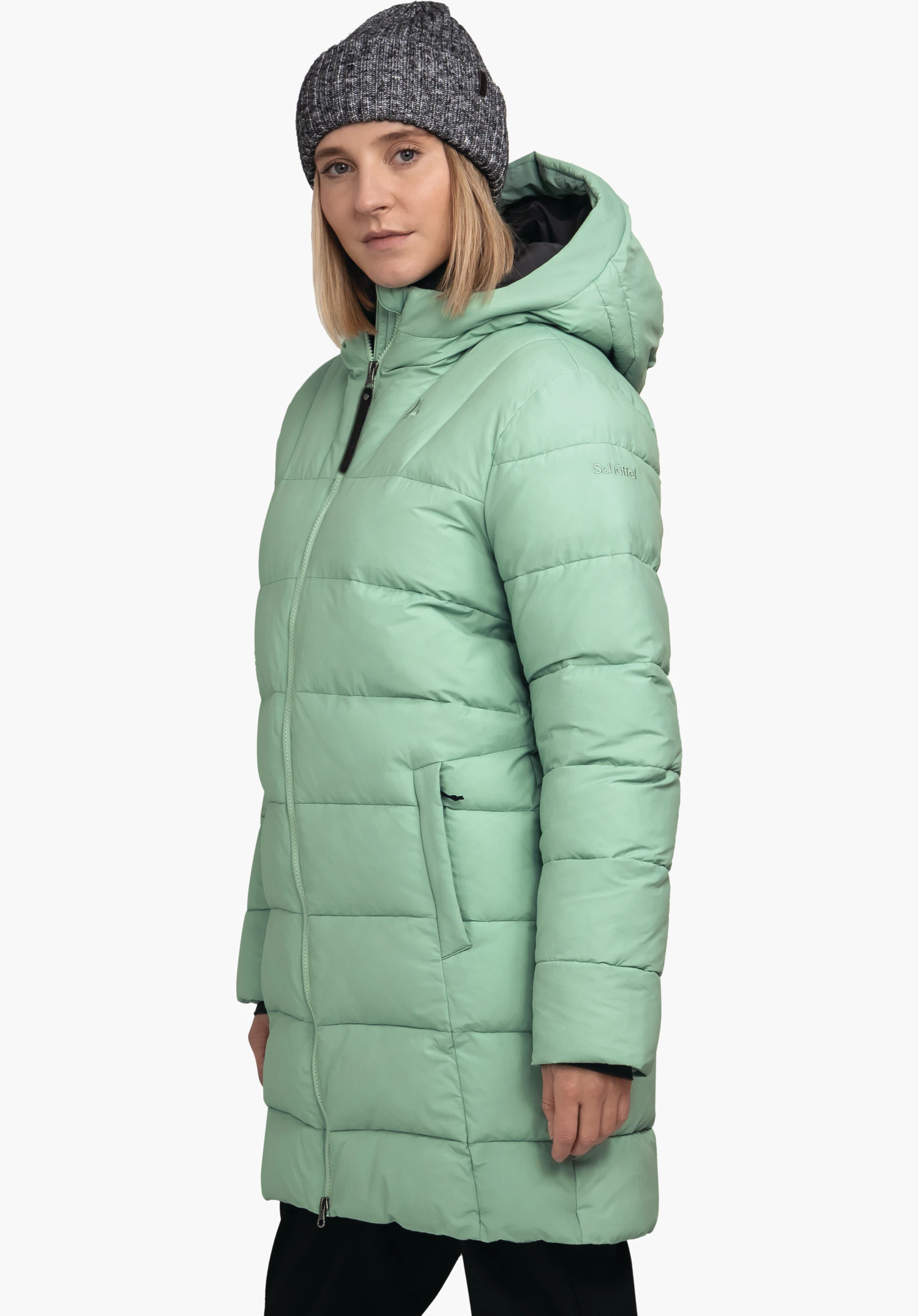 Ins Parka Style Boslix WMS manteau matelassé vert clair porté par une personne en vue trois quarts; capuche en place, fermeture éclair fermée; contexte: fond blanc neutre. Texte sur la manche: "Schöffel".