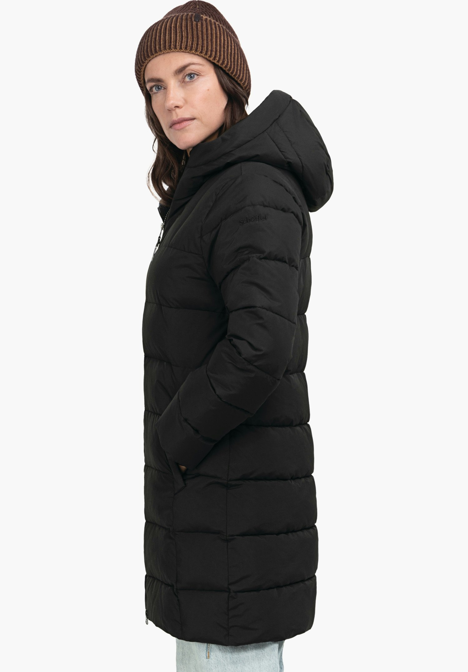 Ins Parka Style Boslix WMS woman wears a black quilted coat with hood, stands side-on with hands in pockets, looks slightly forward in front of a light neutral background. Text on sleeve: "Schöffel".