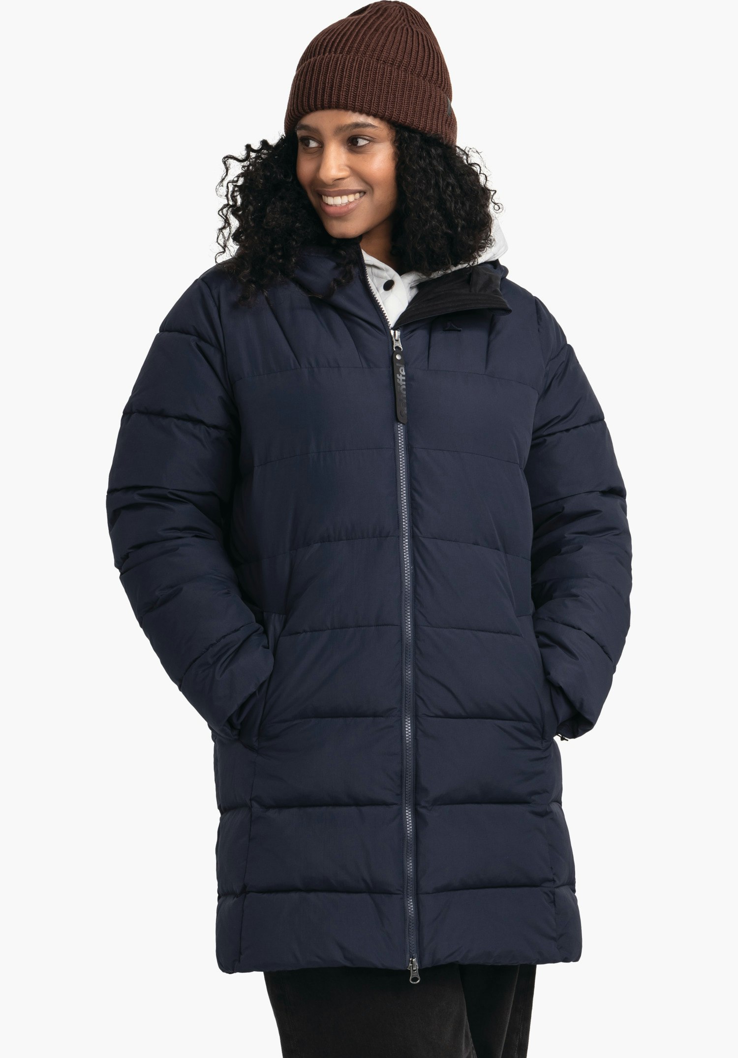 Ins Parka Style Boslix WMS dark blue quilted jacket worn by a smiling person with hands in pockets; triangular Schöffel logo on the chest; white inner hood visible; bright studio background.