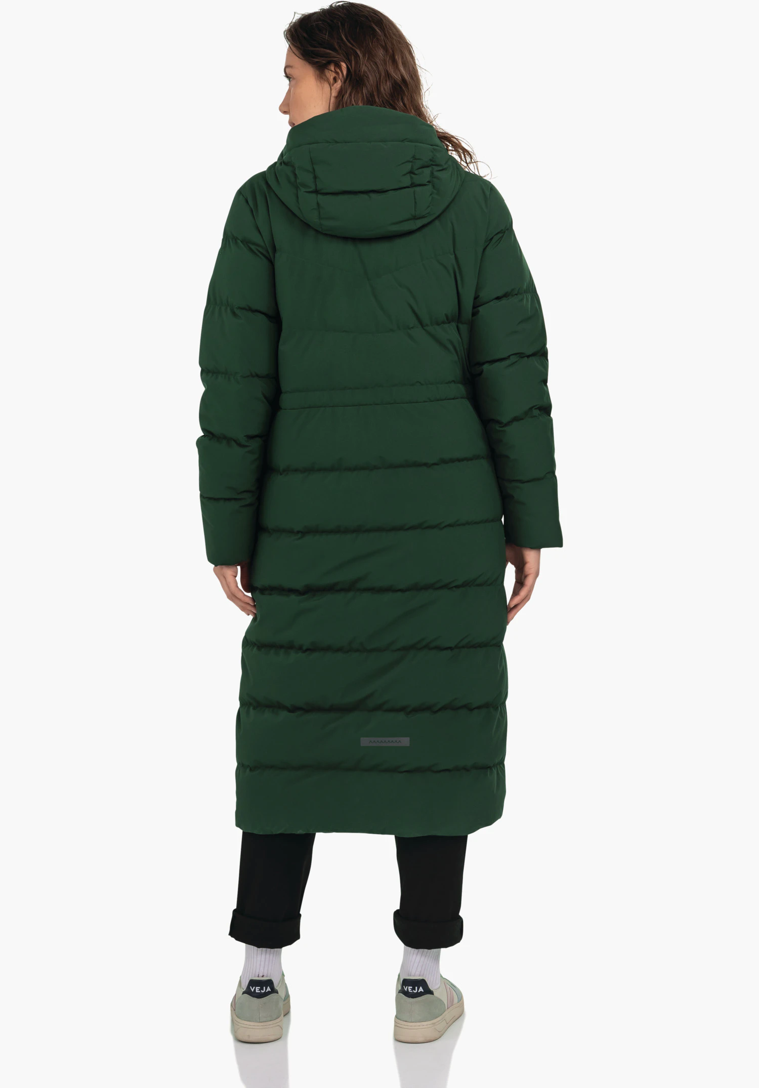Down Coat Style Vindave WMS donkergroene lange gewatteerde mantel, van achteren gedragen door een staande persoon; zwarte broek, witte sokken en sneakers met opschrift "VEJA"; neutrale witte studioachtergrond.